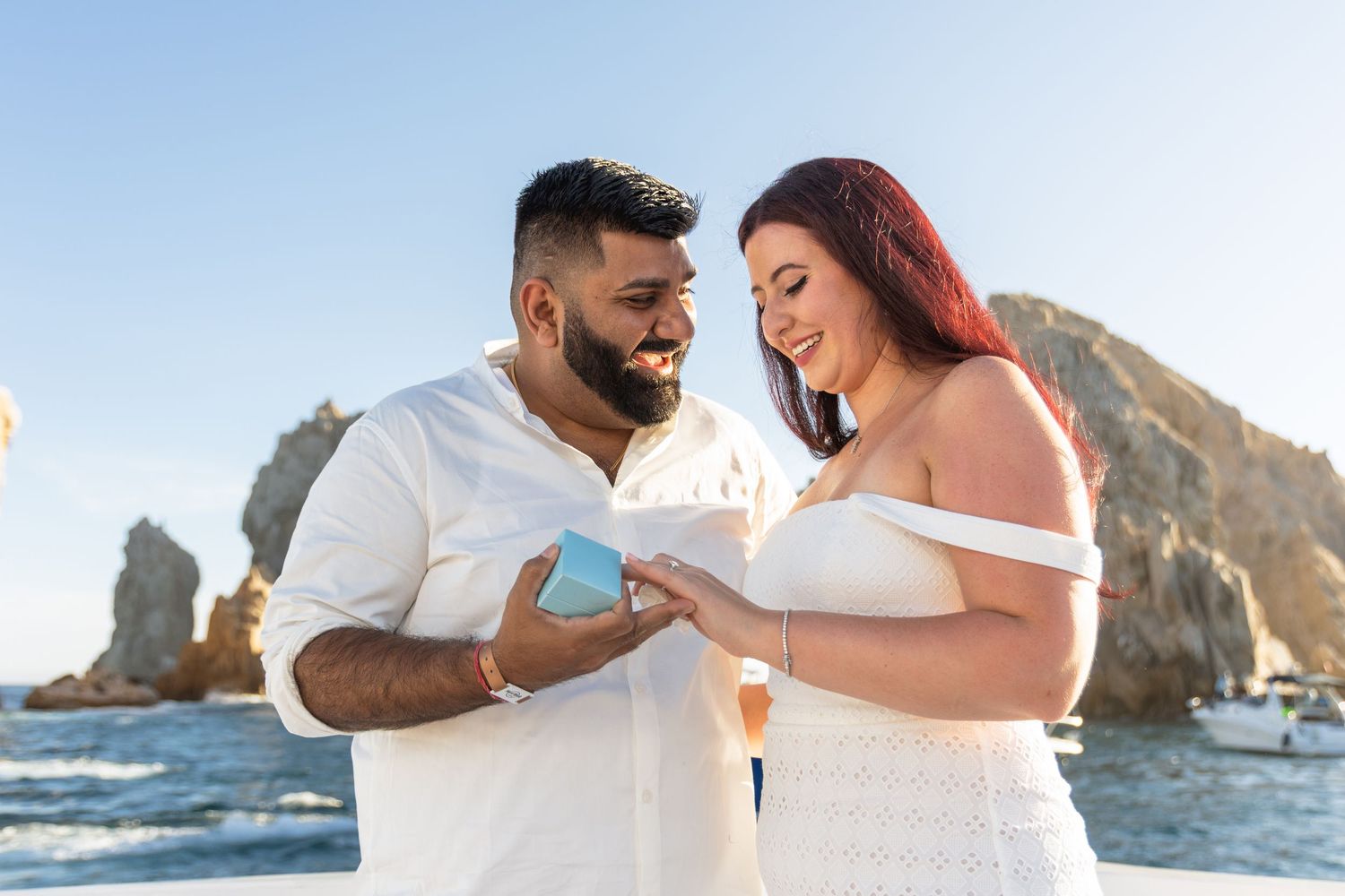 A romantic couple sharing a joyful moment together with El Arco rock formation in Cabo San Lucas as backdrop.