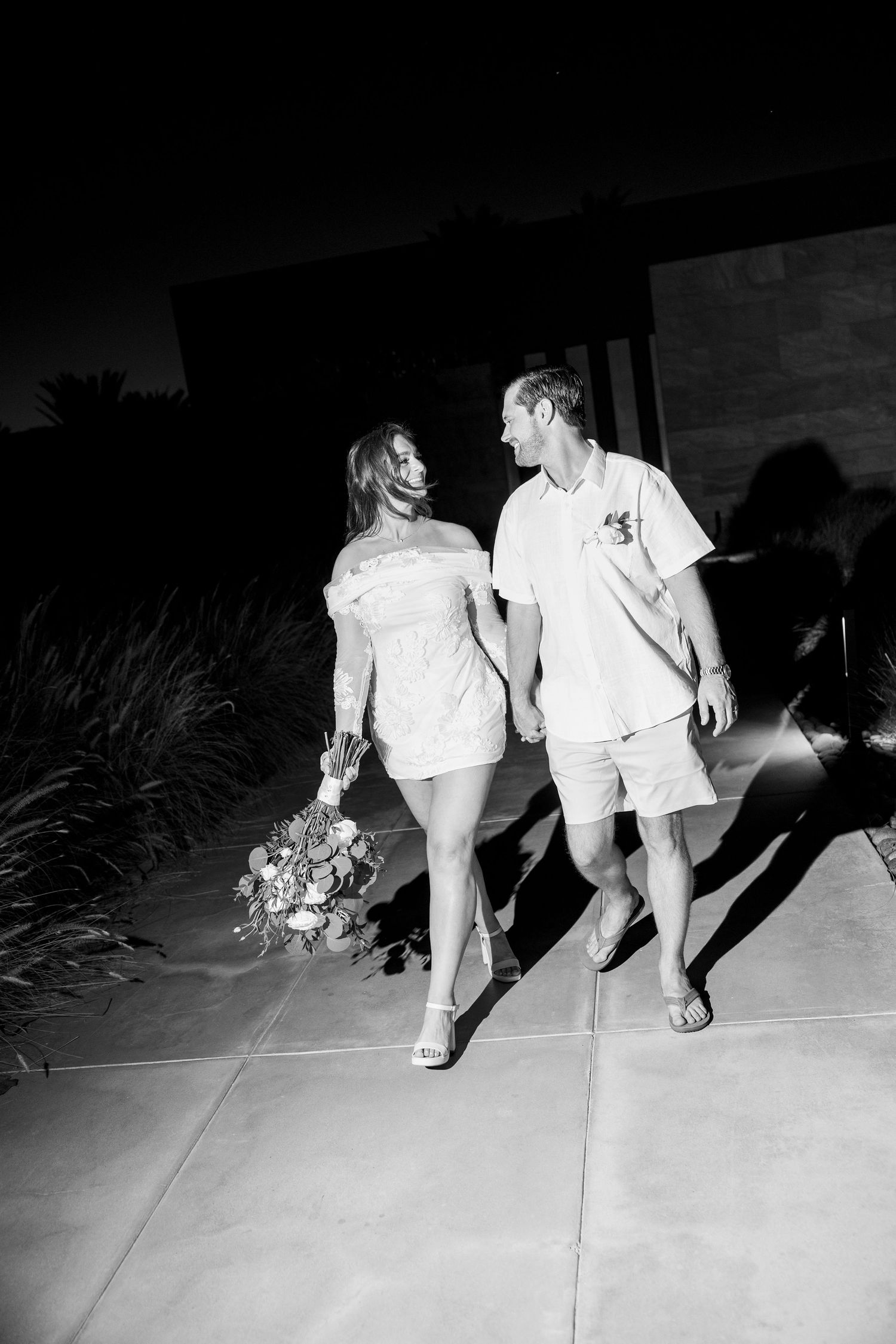 Black and white photo of couple walking on concrete path at night with dramatic shadows.