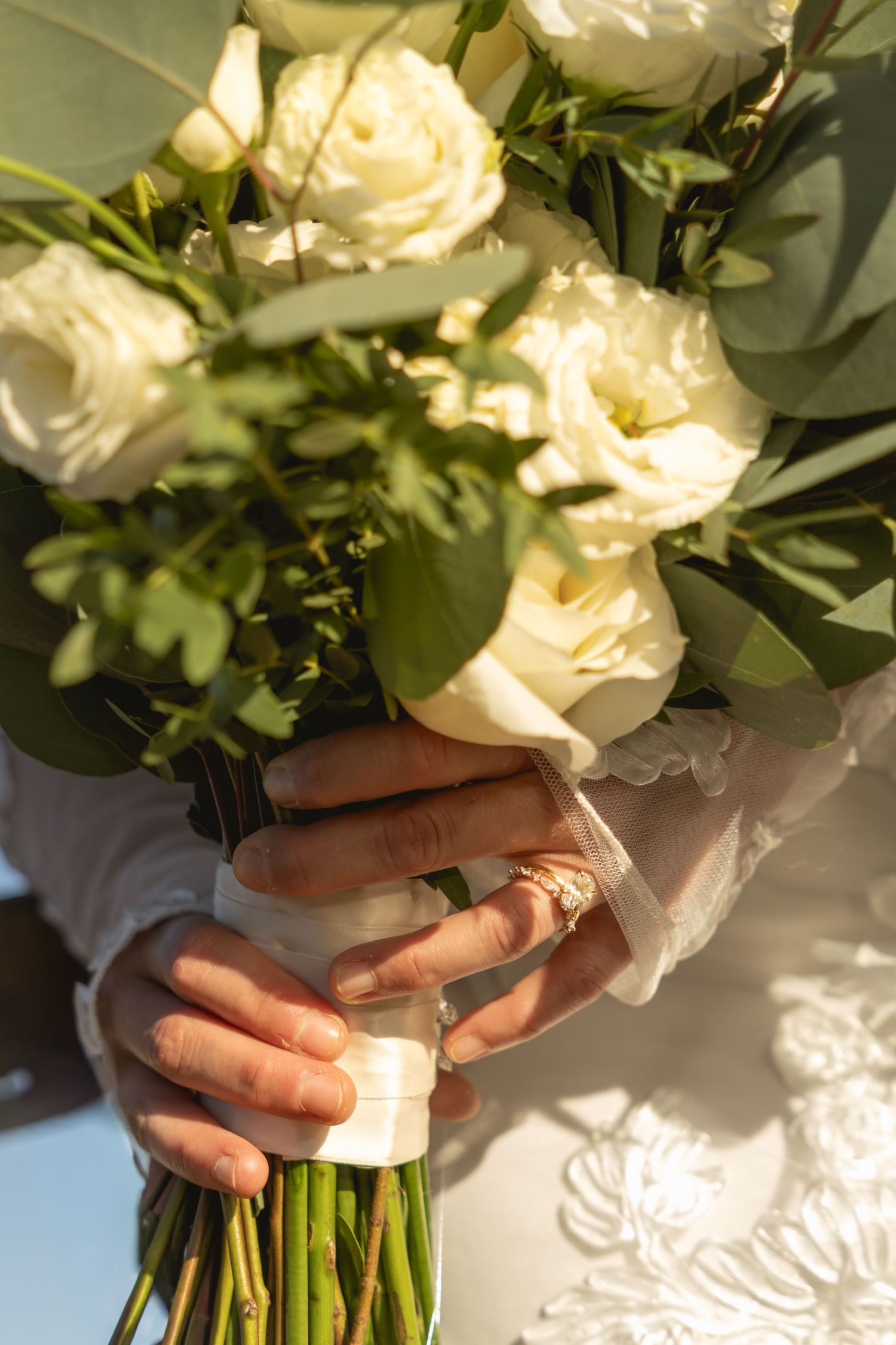 Hands holding a beautiful bouquet of white roses and greenery in natural sunlight.