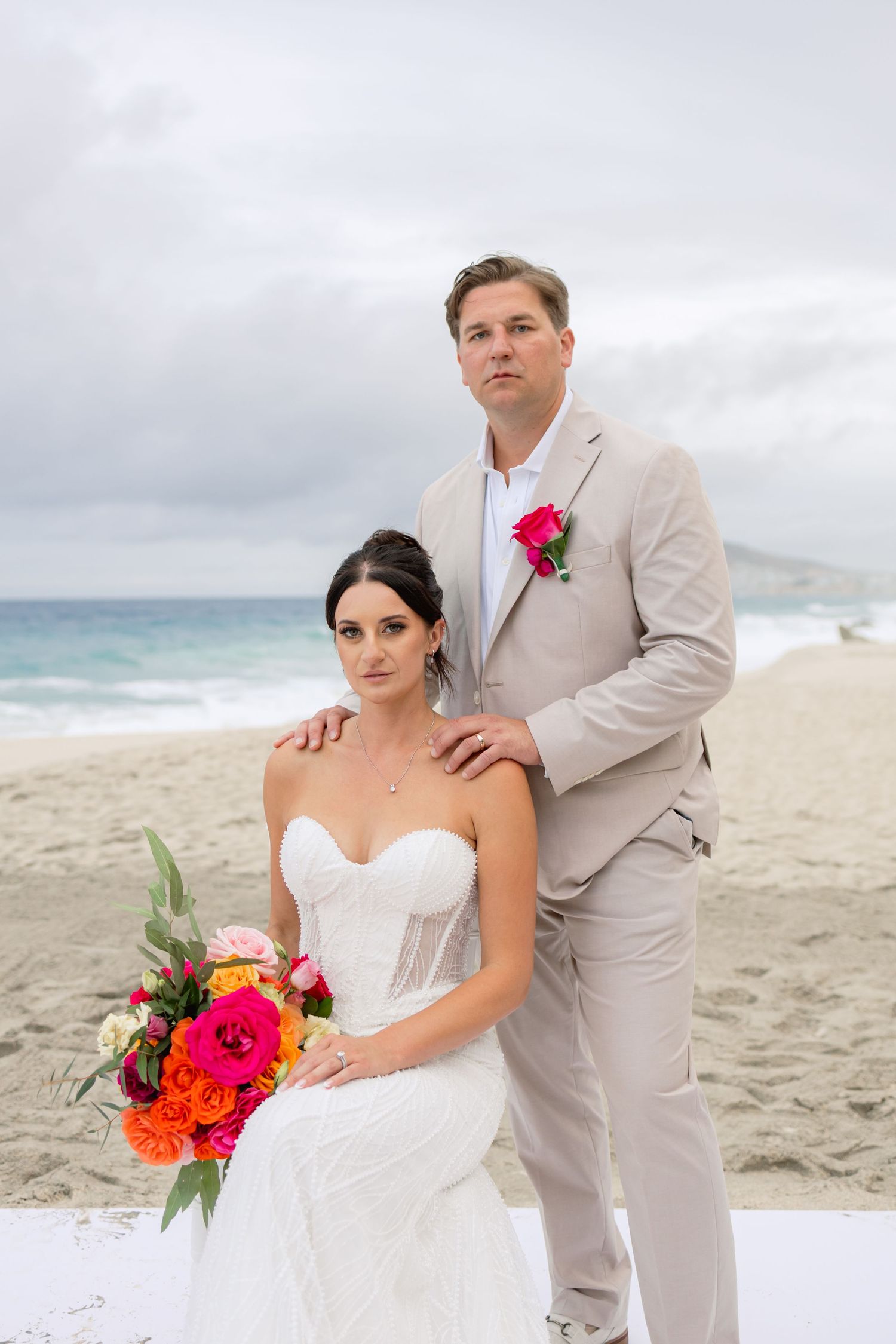 Beachside wedding portrait with couple in light colored attire against cloudy sky.