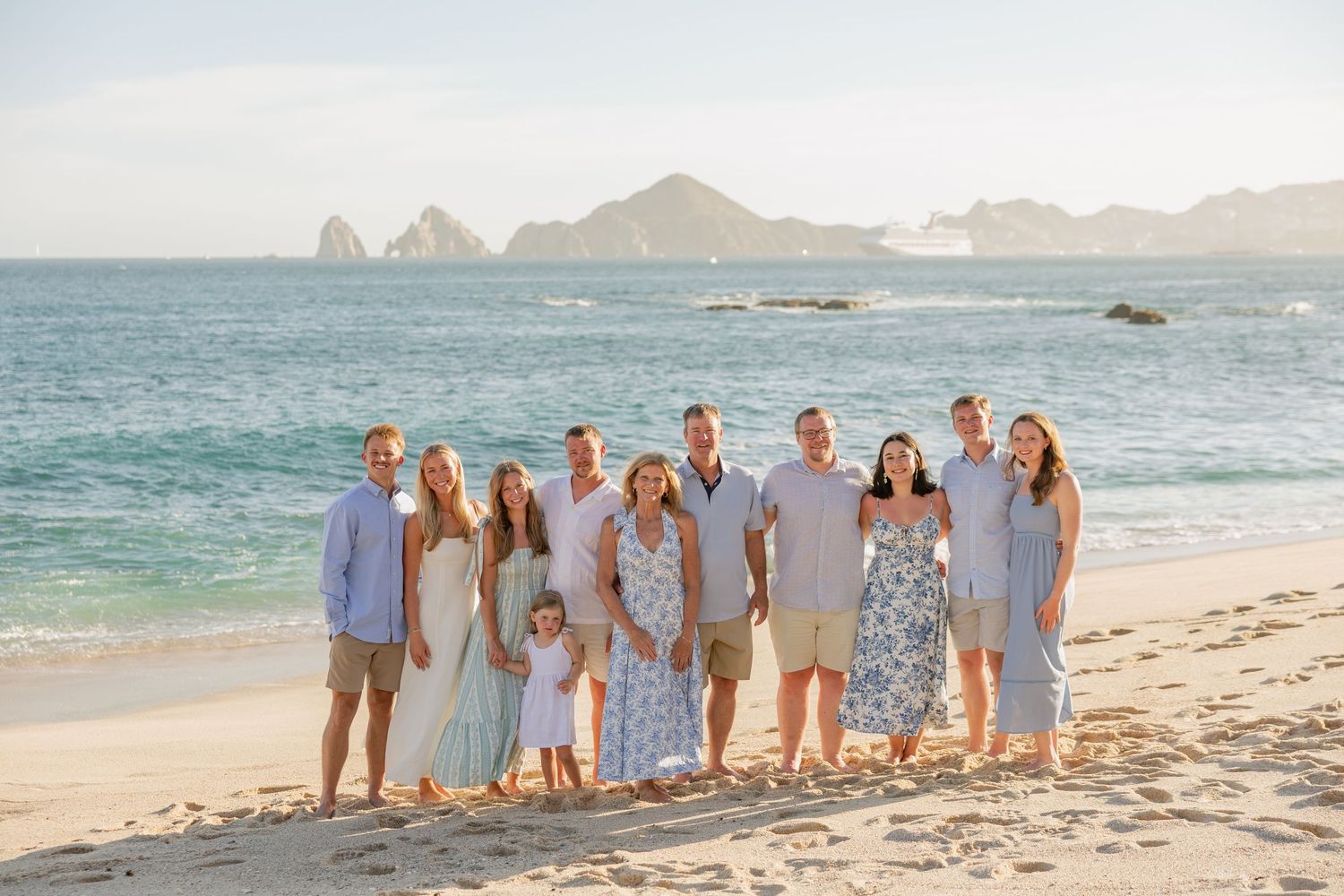 Large family group posing together on a sunny beach in Cabo San Lucas with iconic rock formations in the background.