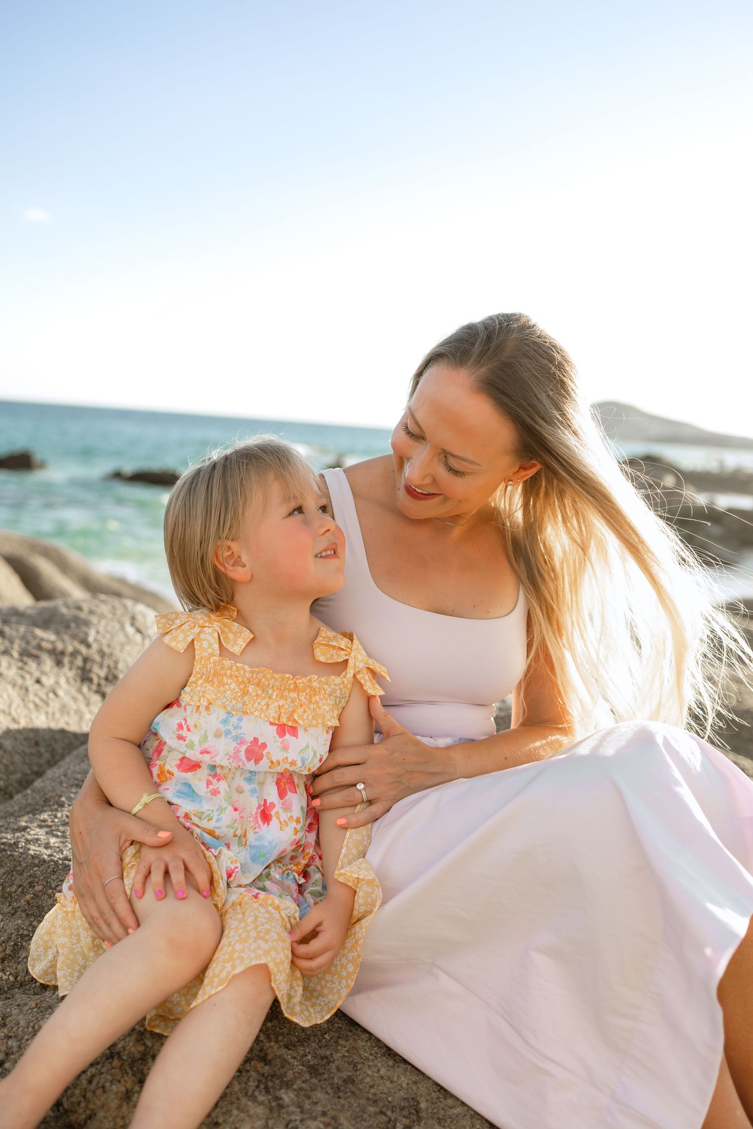 Mother and daughter share tender moments together on a sunny beach while wearing white and floral outfits at Garza Blanca, Los Cabos