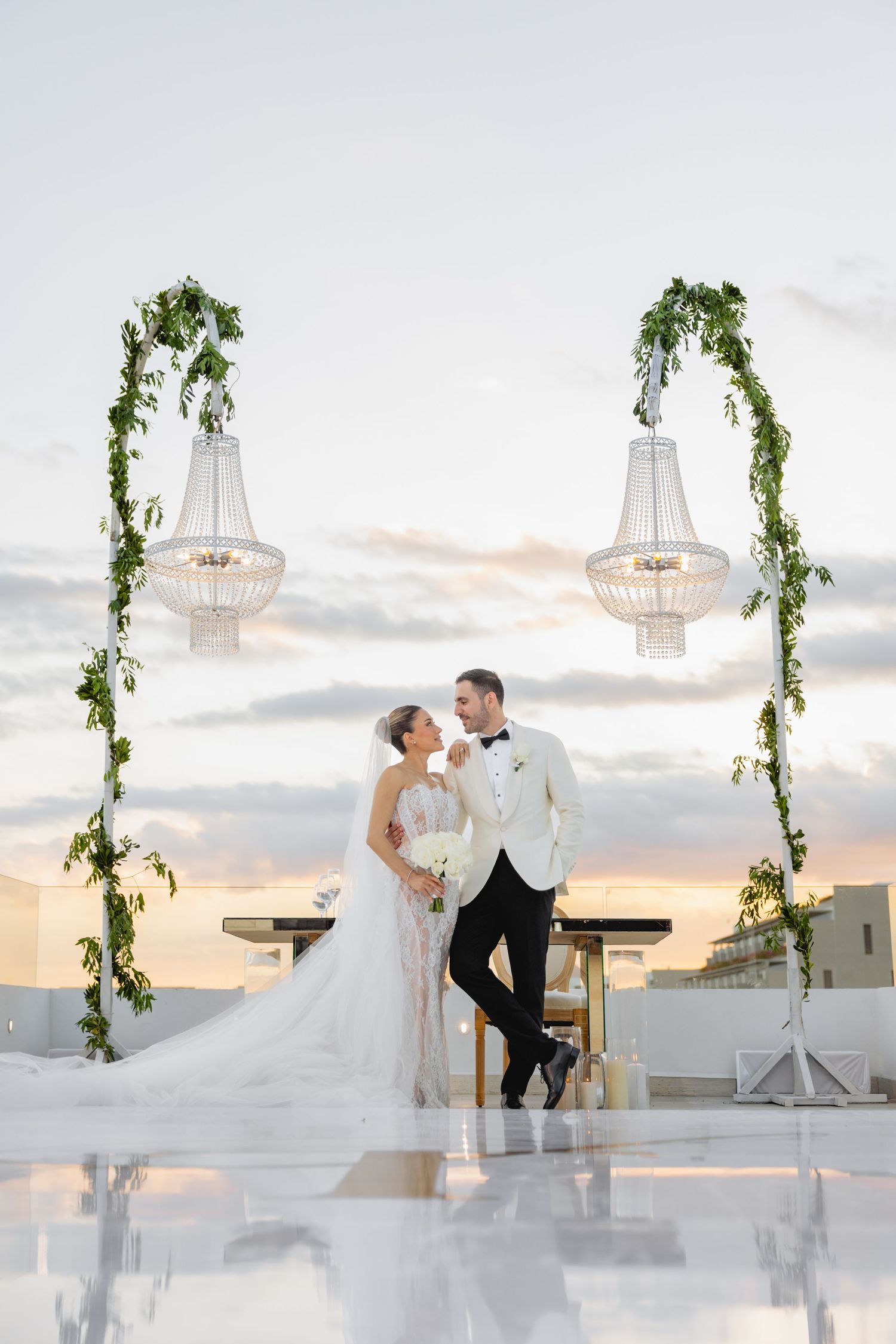 Romantic sunset rooftop wedding ceremony with white decor and hanging greenery.