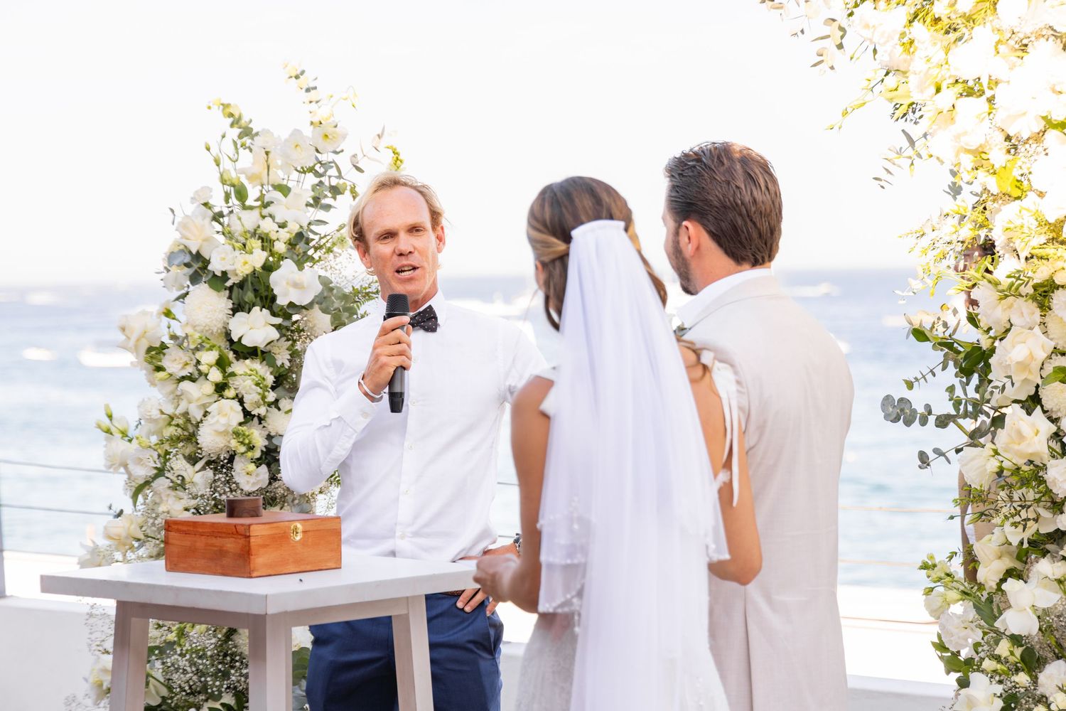 An outdoor wedding ceremony with white floral arrangements and ocean views in the background.