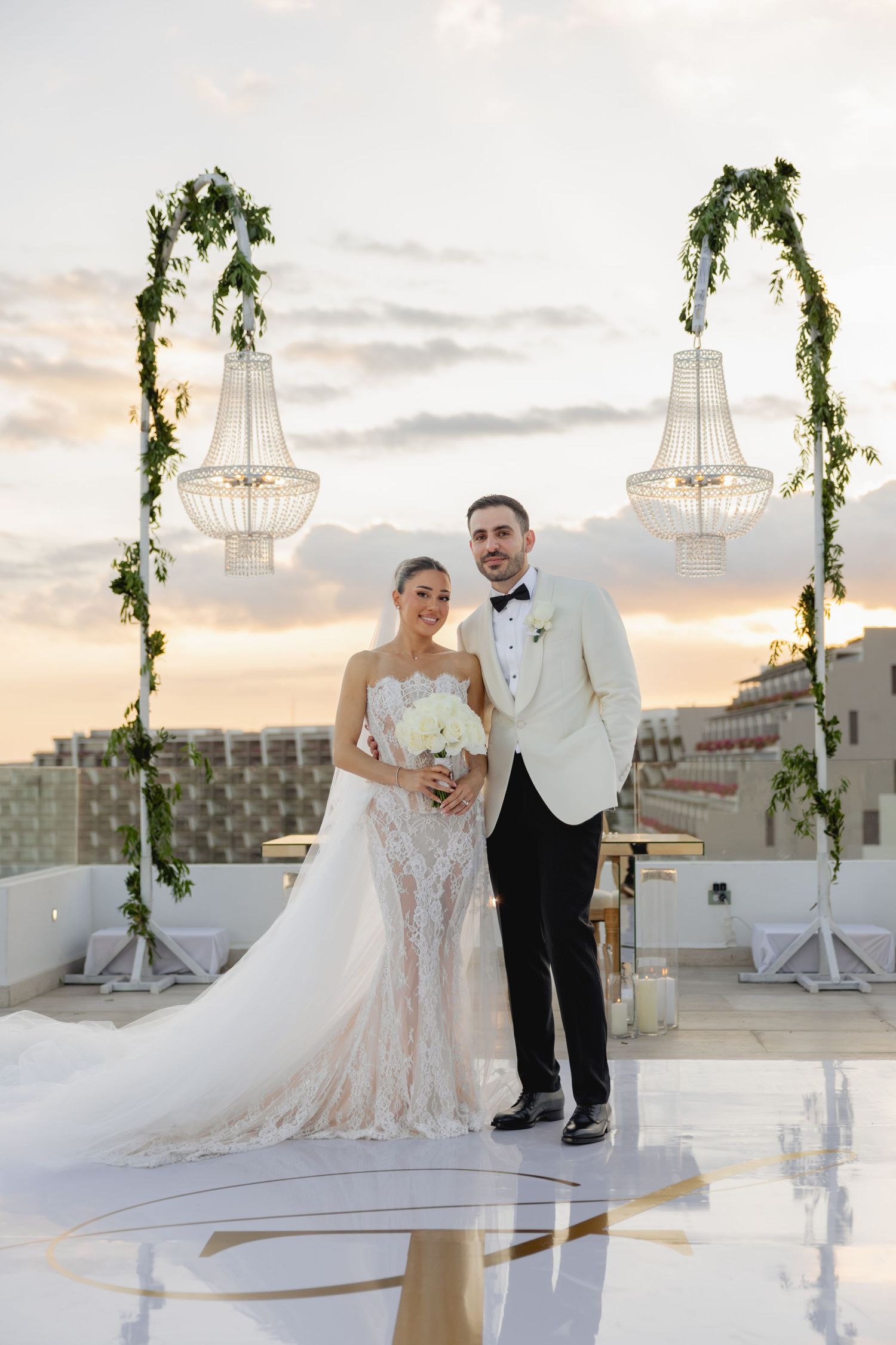 Elegant rooftop wedding venue decorated with hanging lanterns and greenery against sunset sky.