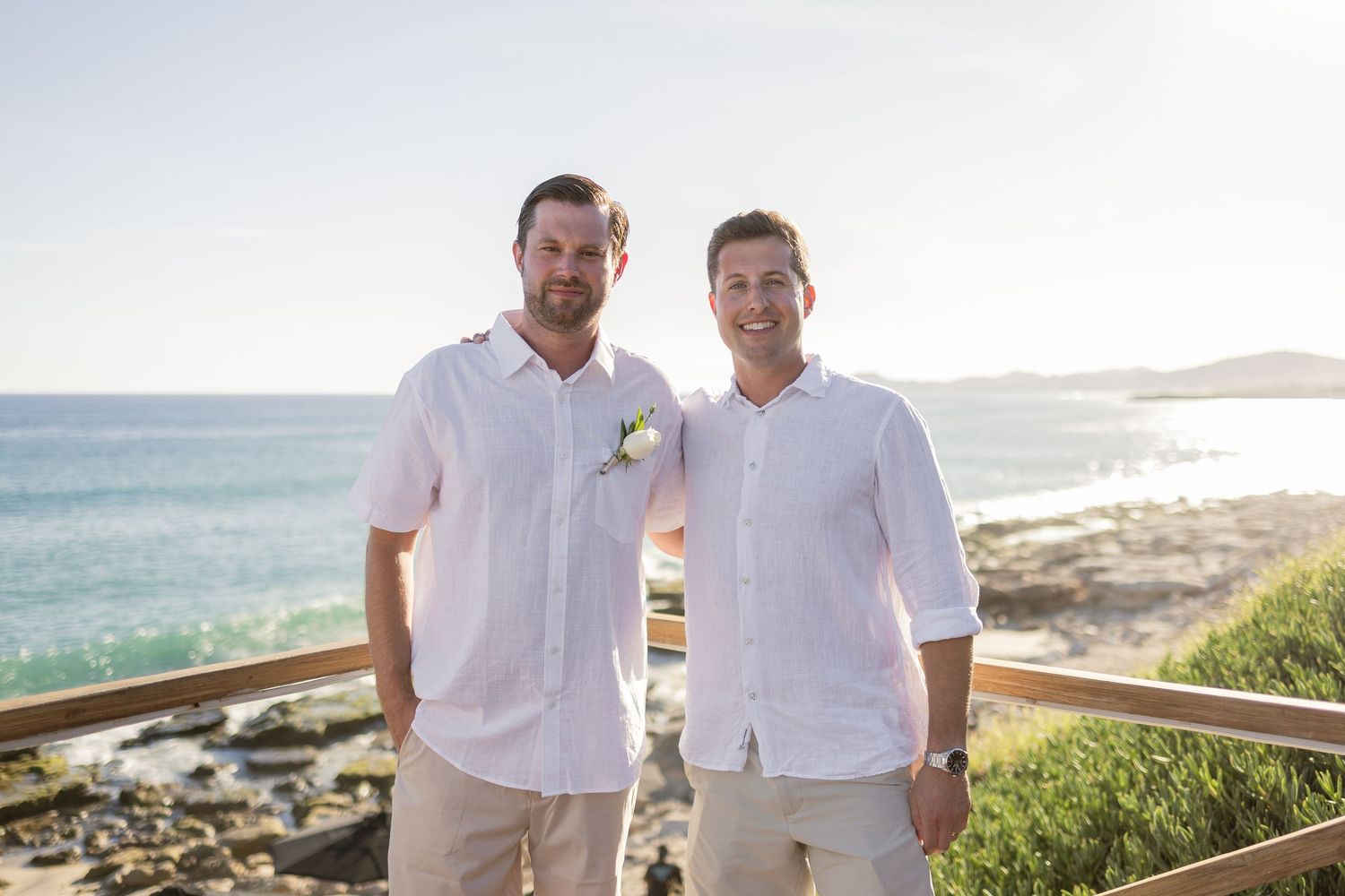 Wedding party members in white attire gather on a scenic oceanfront deck.