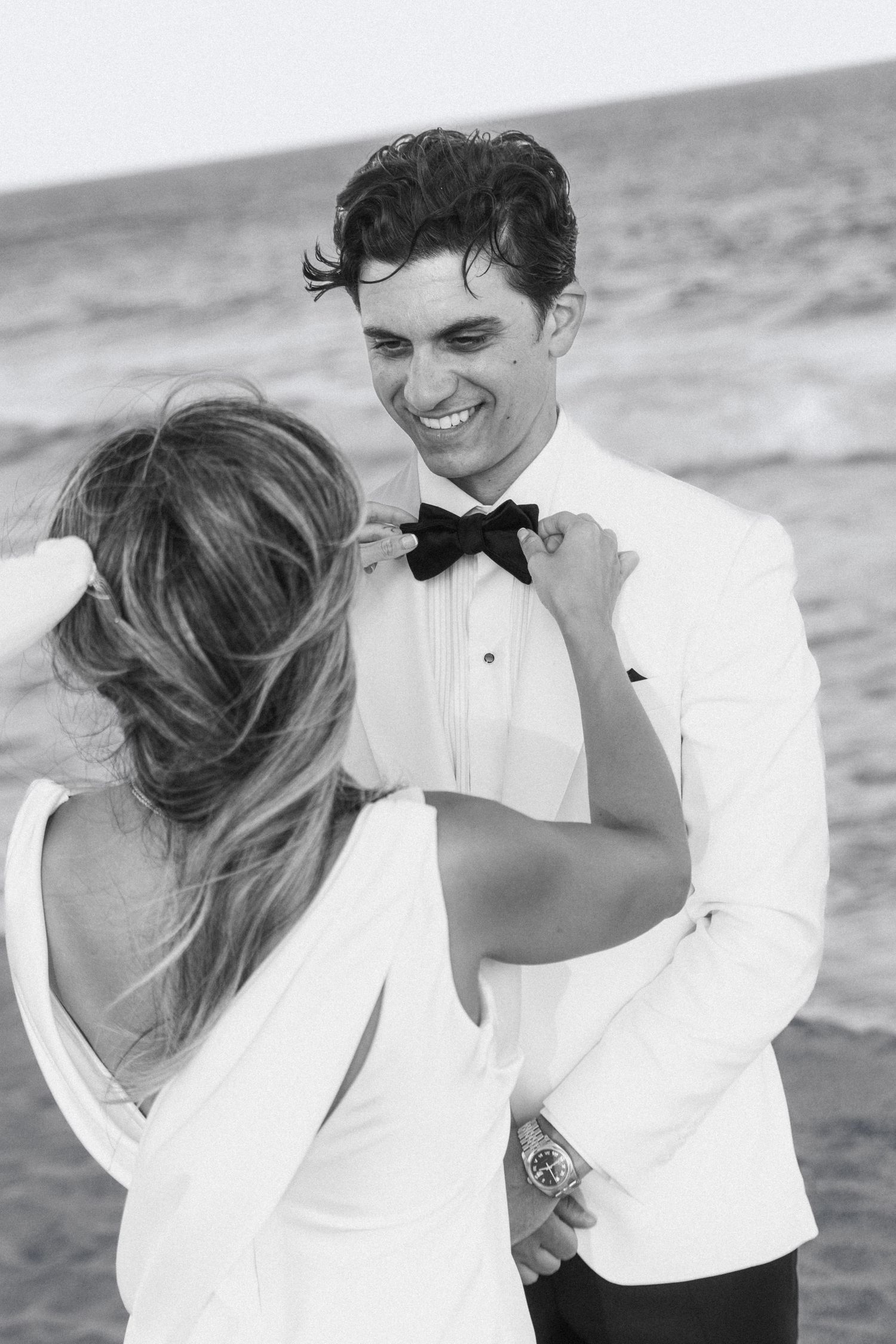 Romantic black and white beach wedding photos showing couple embracing and laughing together by the ocean.
