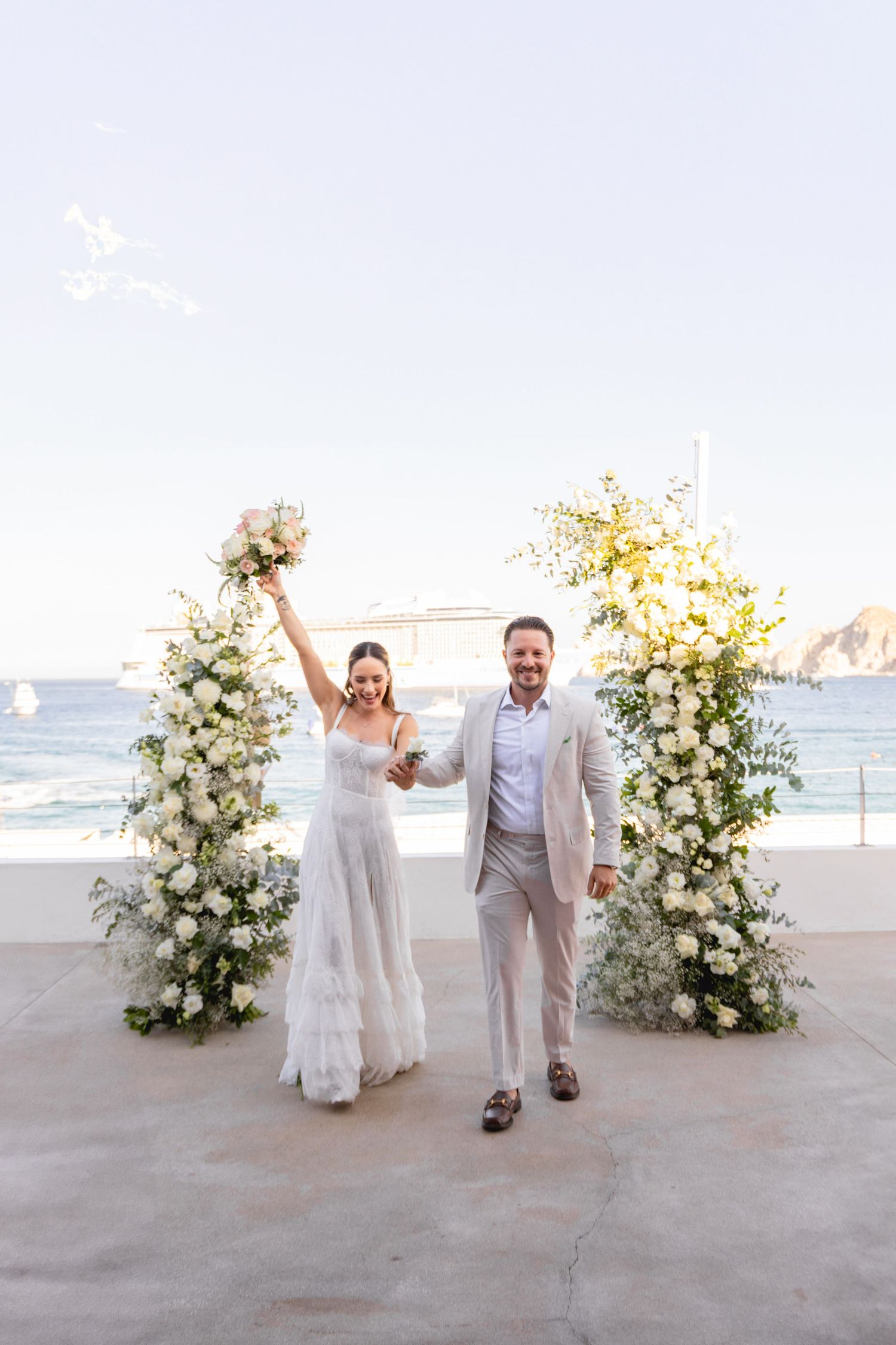 Wedding ceremony setup with white floral arches and ocean view.