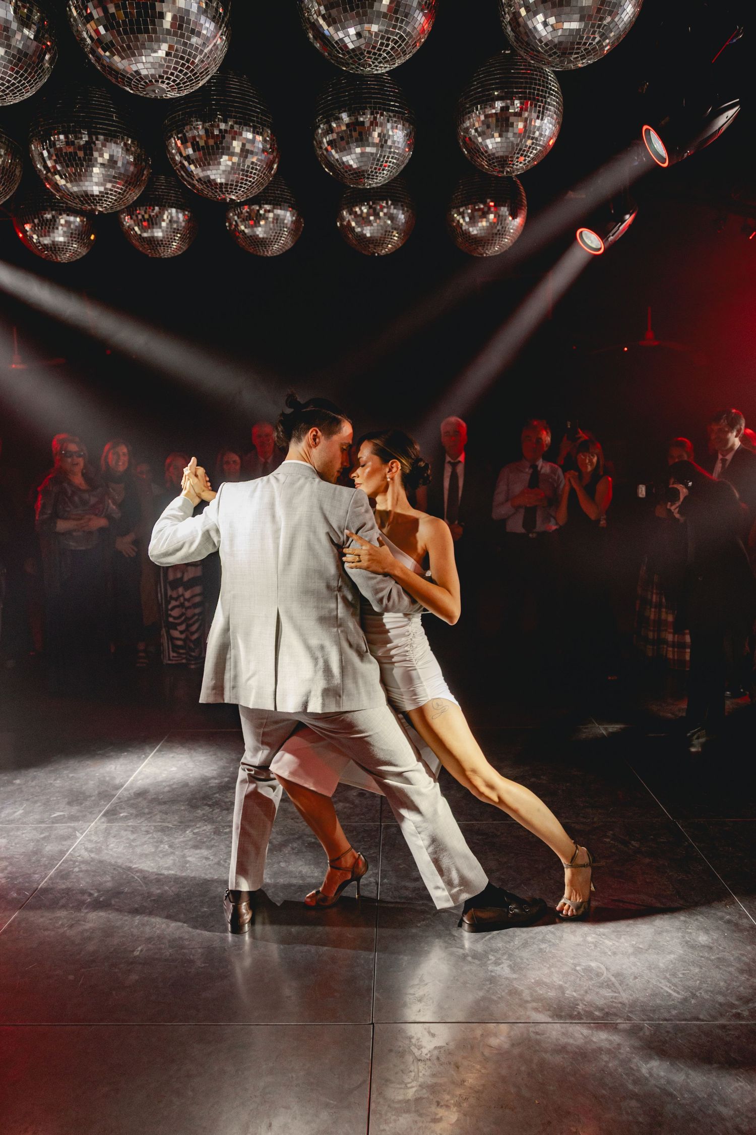 Dancers perform a dramatic tango sequence under disco balls in a dark ballroom setting.