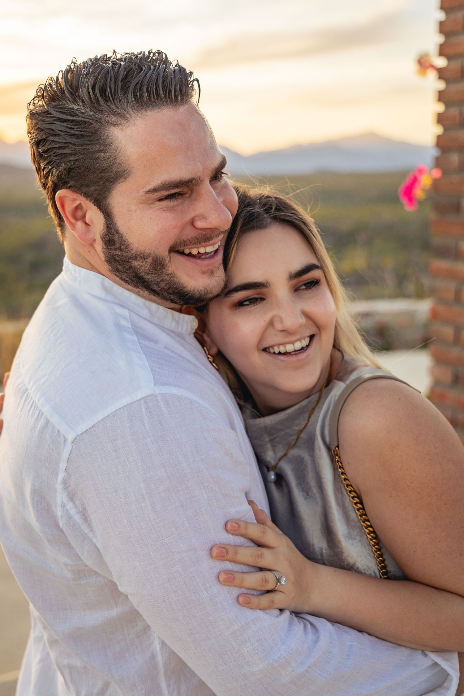 A happy couple embraces and laughs together during a warm sunset in the desert with mountains in the background.