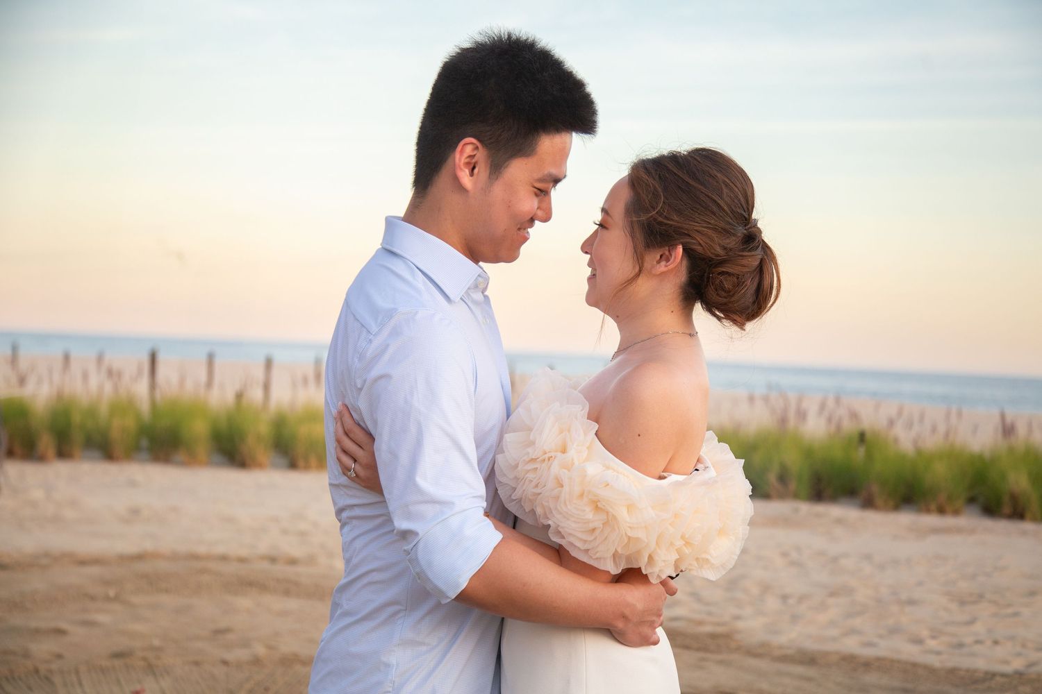 A romantic couple embraces on a sandy beach at sunset with soft golden light illuminating the scene.