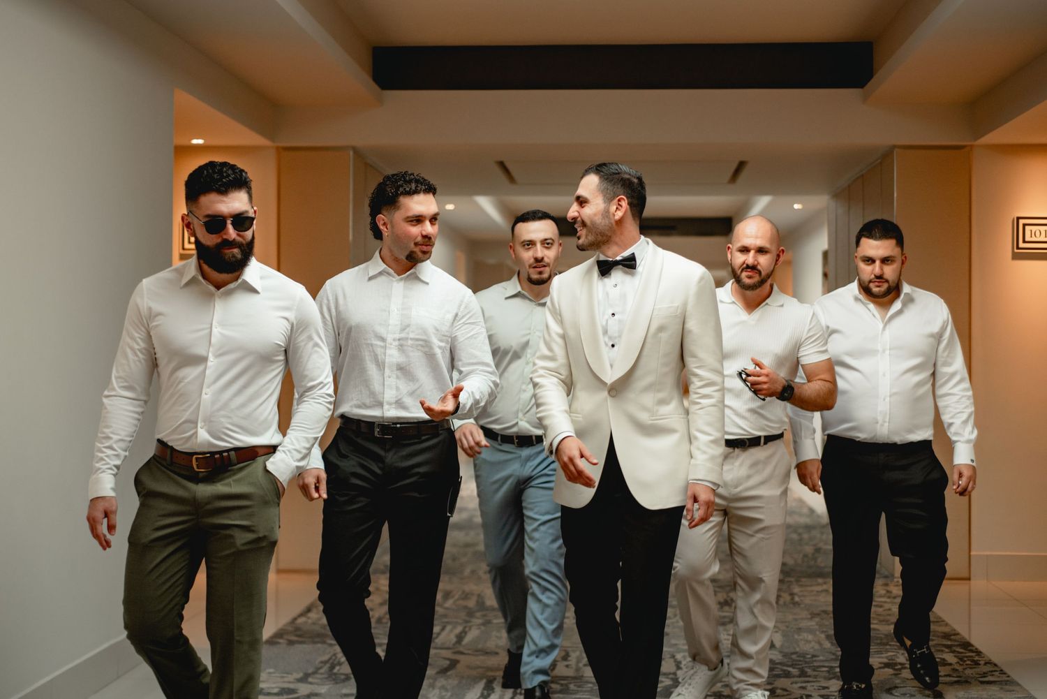 Groomsmen in formal attire walking and posing in an indoor venue.