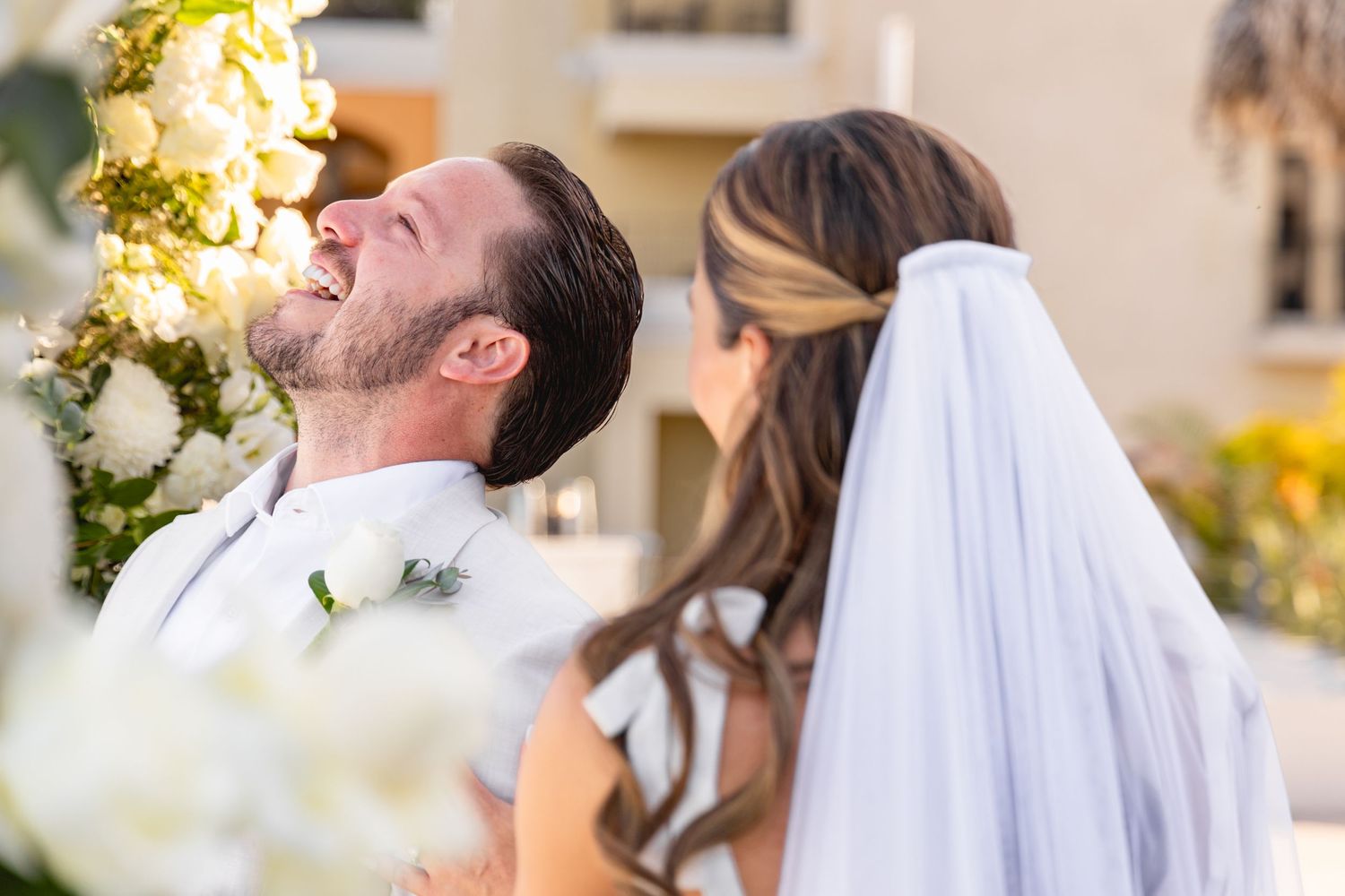 A joyful moment captured during an outdoor wedding ceremony with white and yellow floral decorations.