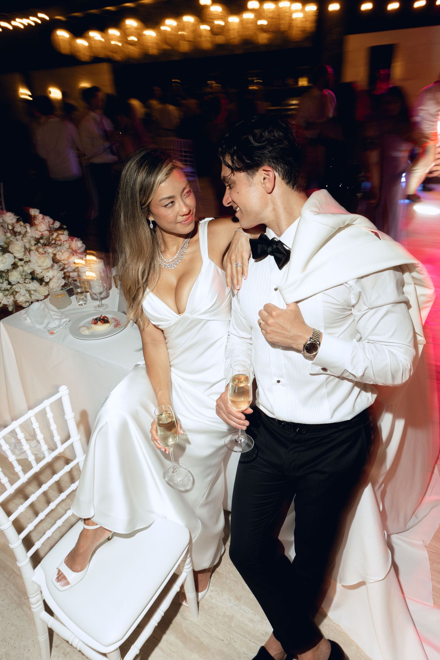 Couples dancing at wedding reception with white chairs and candlelit ambiance.