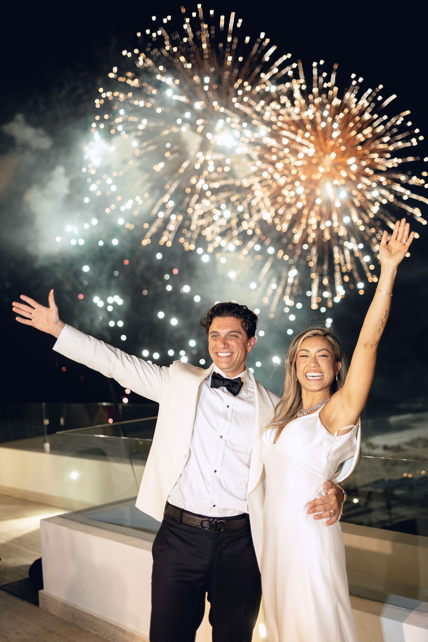 Celebratory moment with fireworks display lighting up the night sky behind couple.