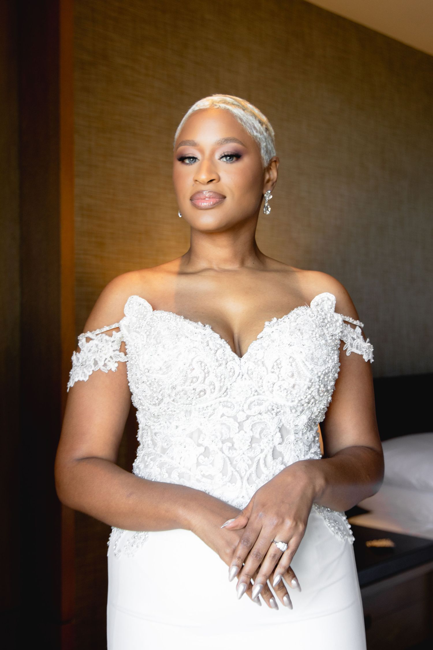 Bride wearing an elegant off-shoulder white lace wedding gown with intricate beading and embroidery details.