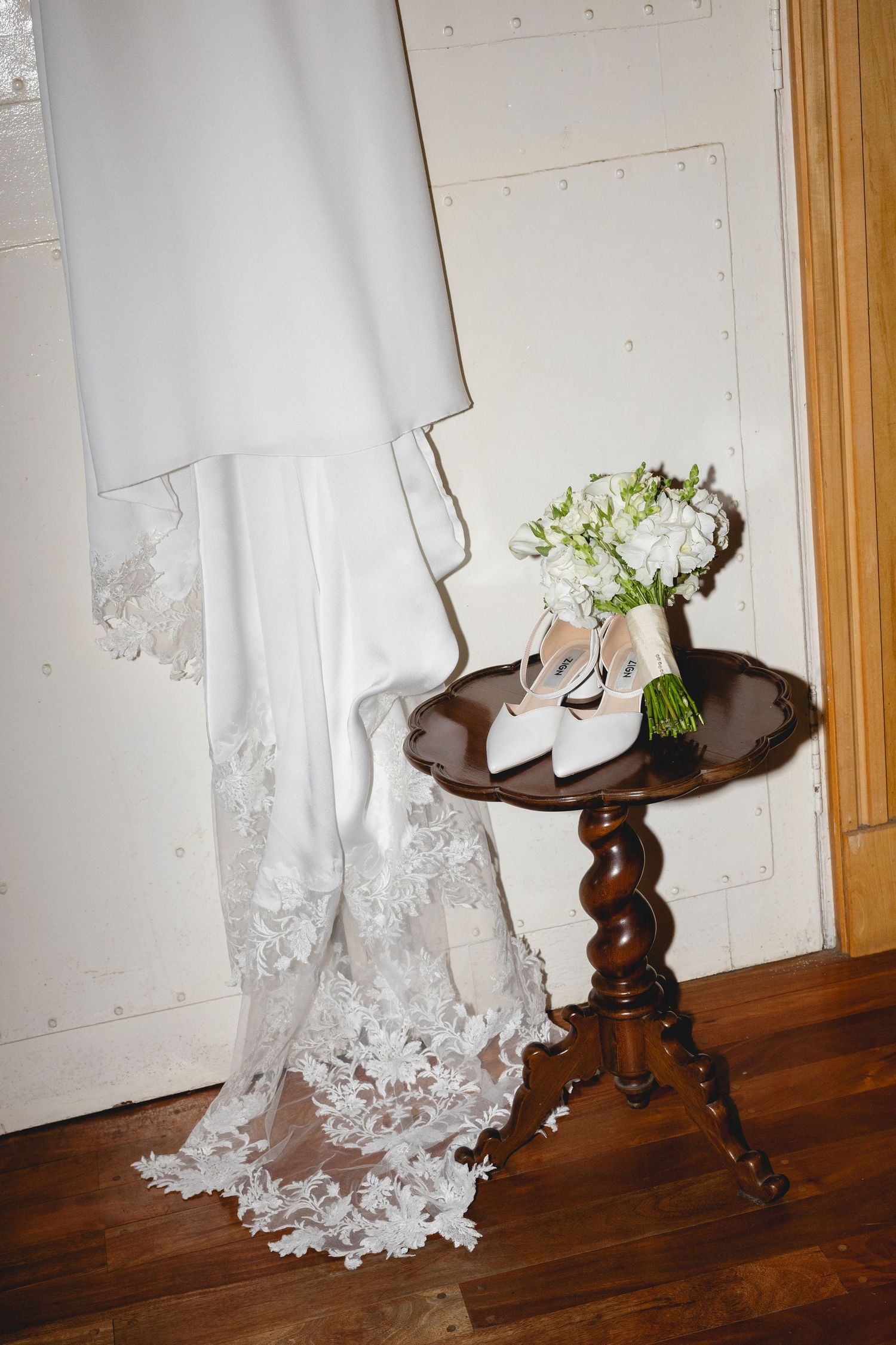 White lace wedding dress detail draped over an antique wooden table.