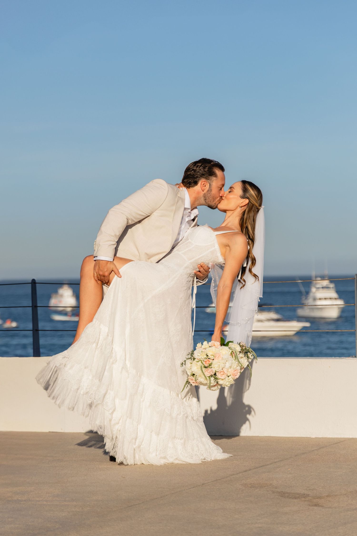 Dramatic wedding dip pose against ocean and boats backdrop.