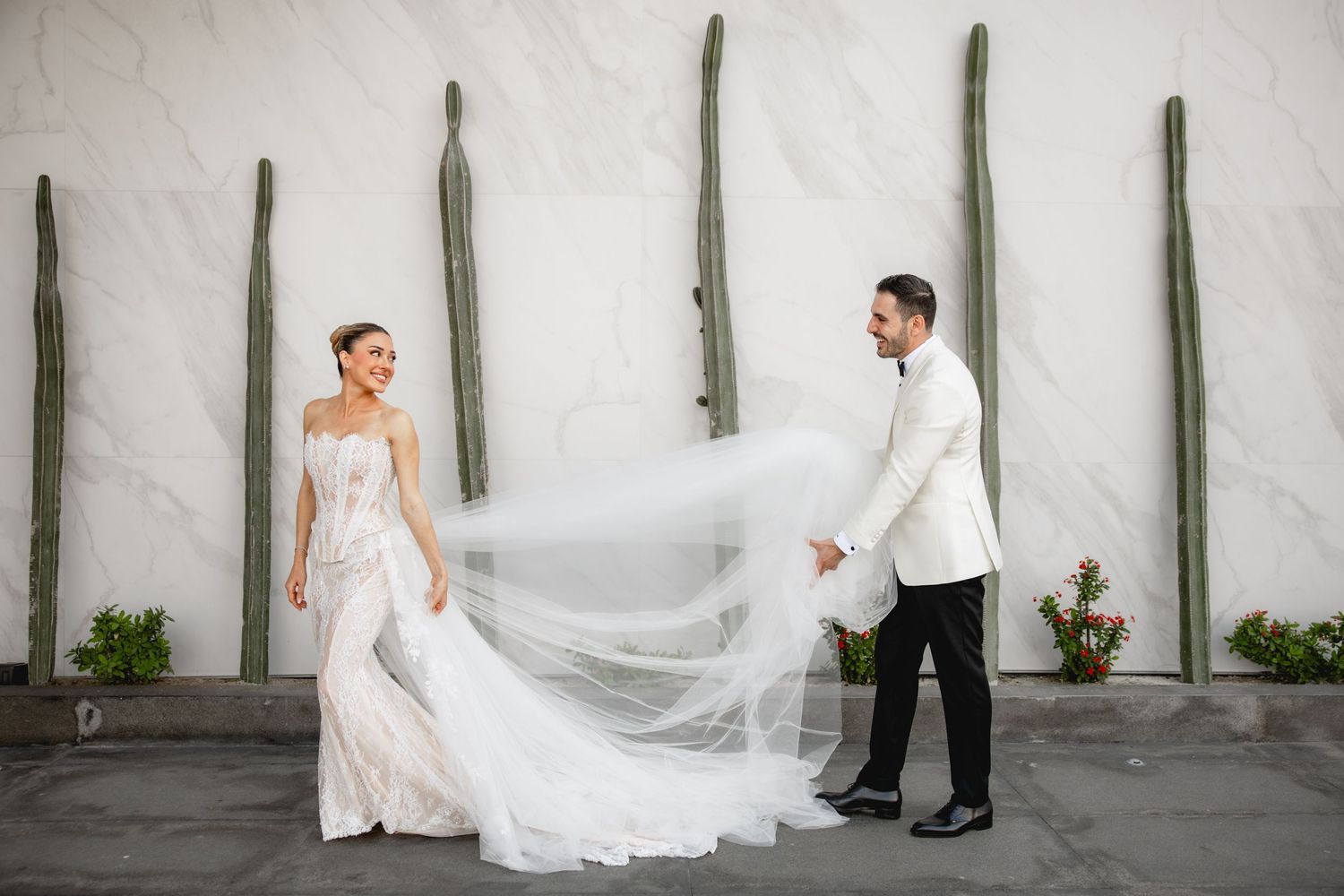 Wedding couple walking along a white wall with vertical green posts in an artistic photo series.