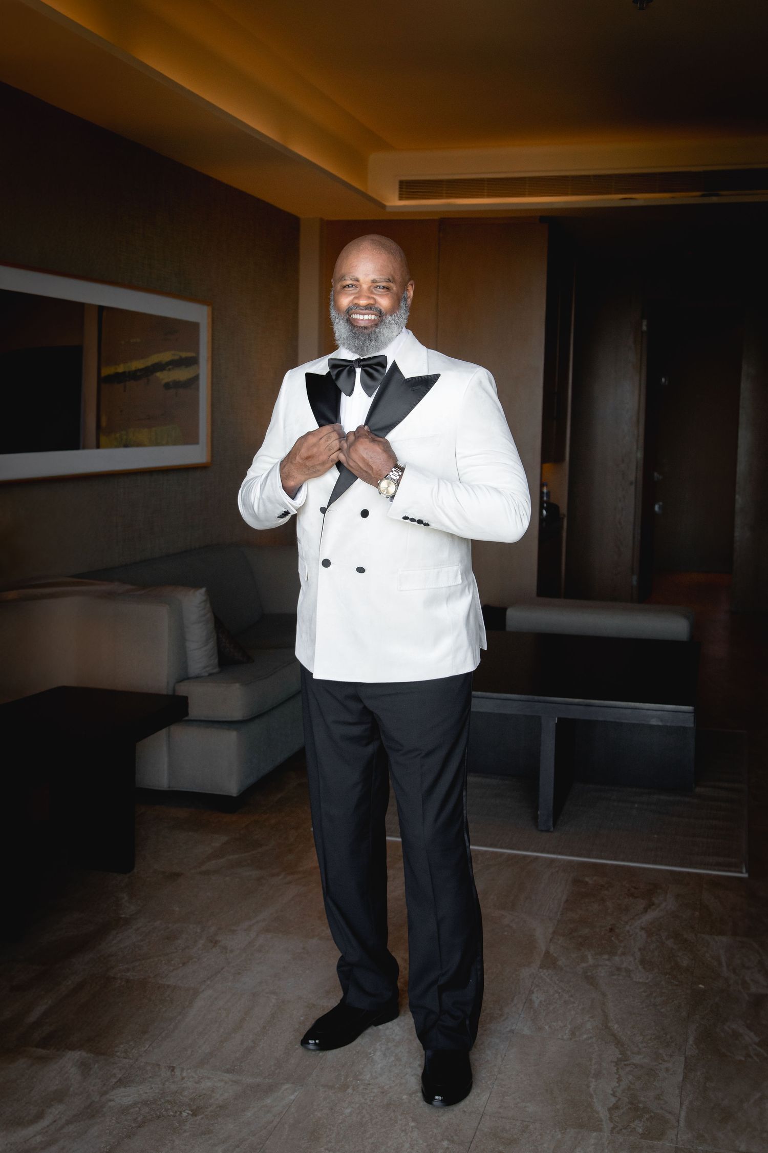 Groom adjusts his white tuxedo jacket in a dimly lit room.