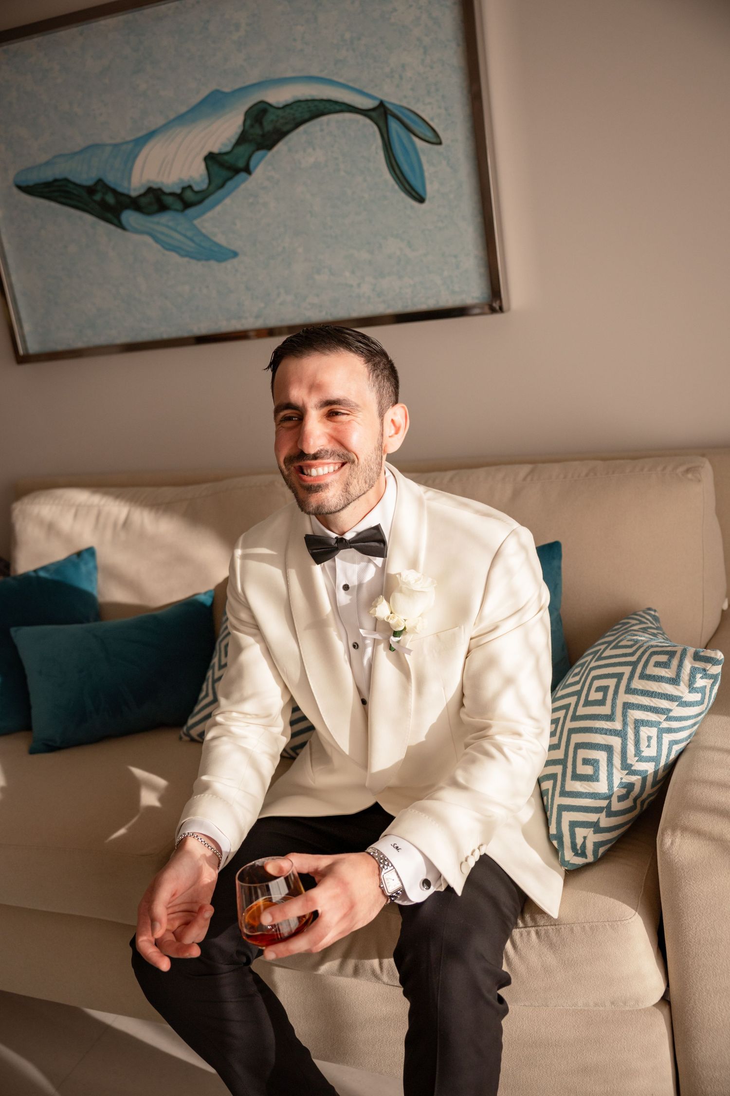 Candid shot of groom laughing while seated on cream colored couch.