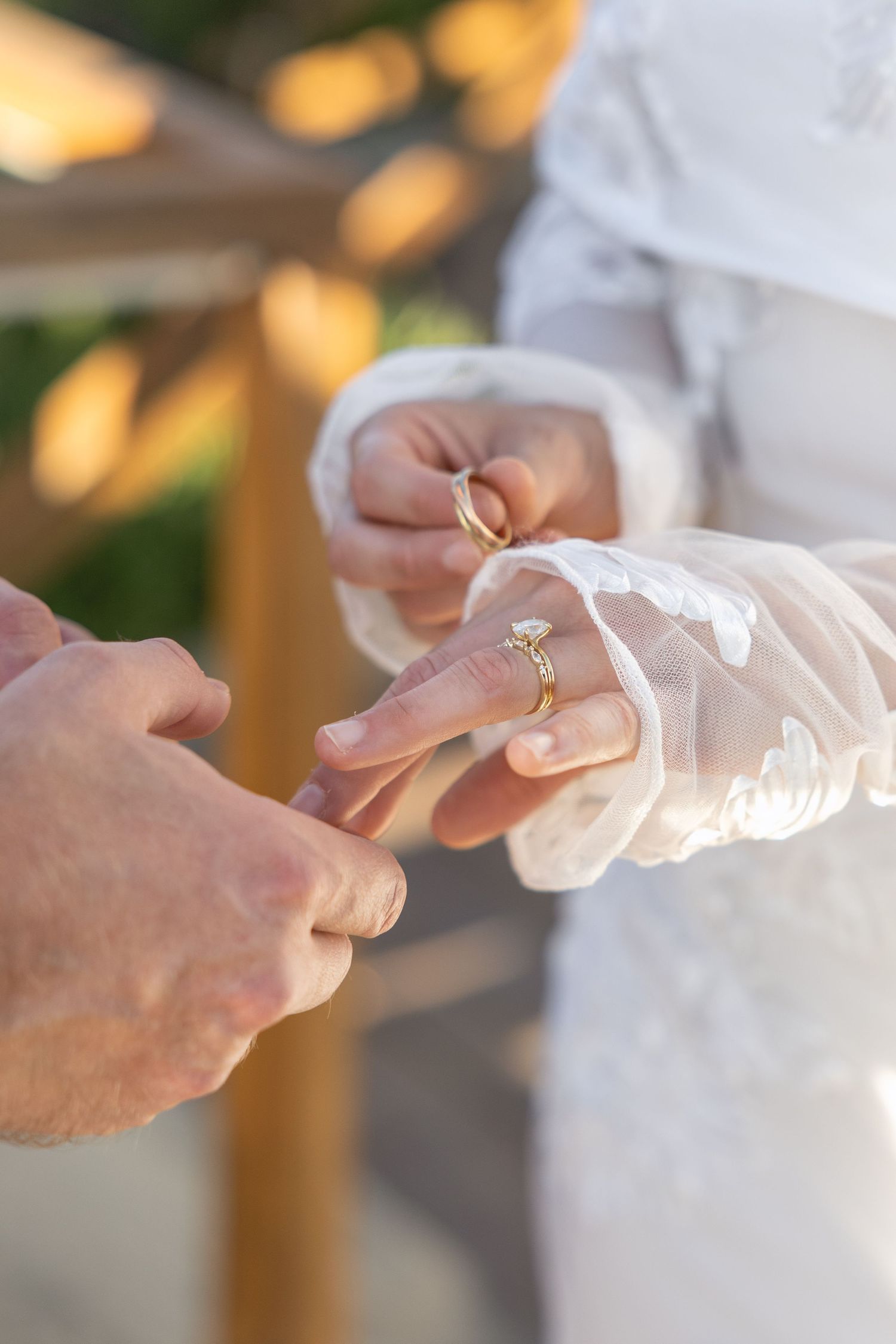 Detailed shot of wedding ring exchange with lace dress in background.