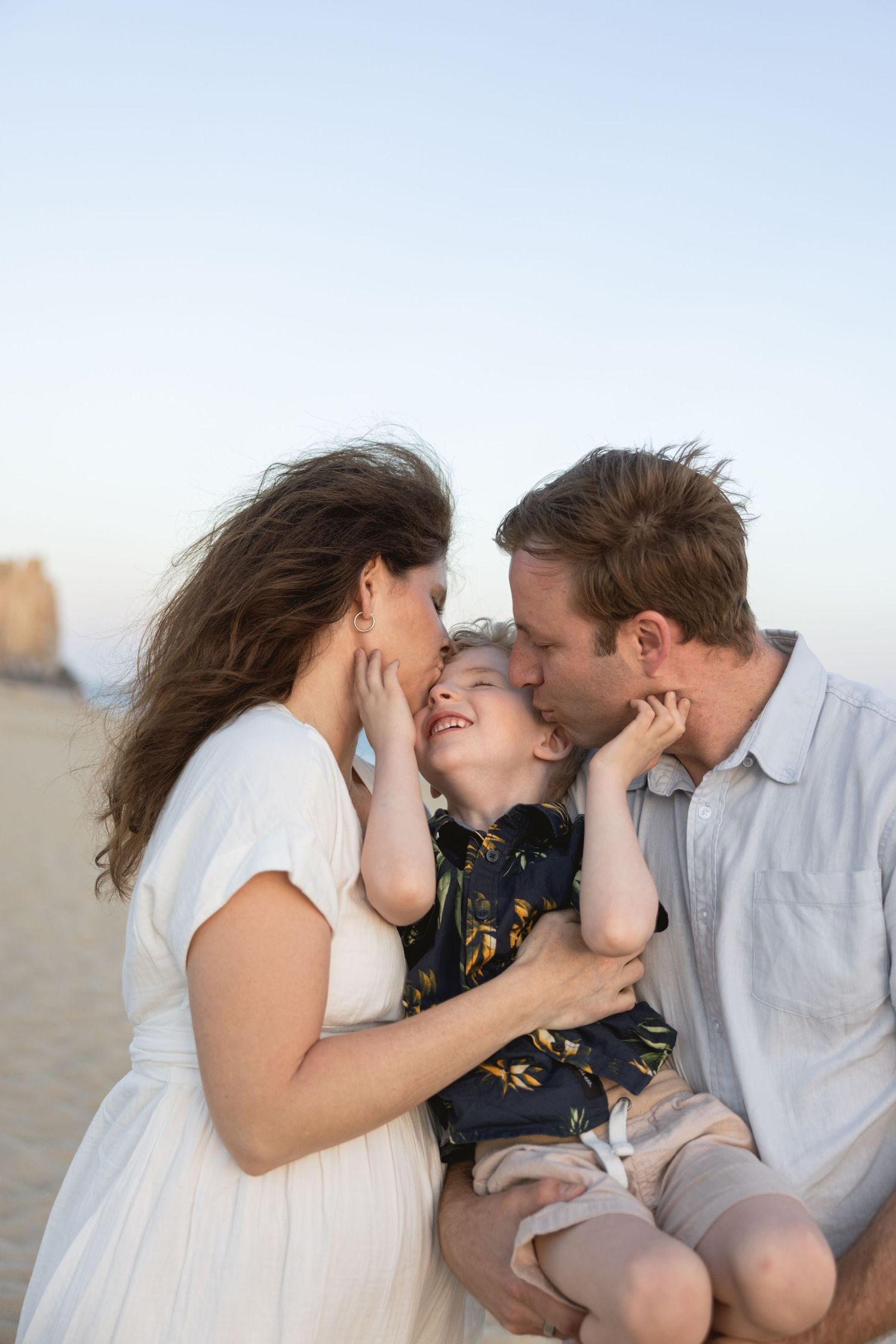 Family sharing tender moments together on a beach during sunset with soft lighting and casual attire.