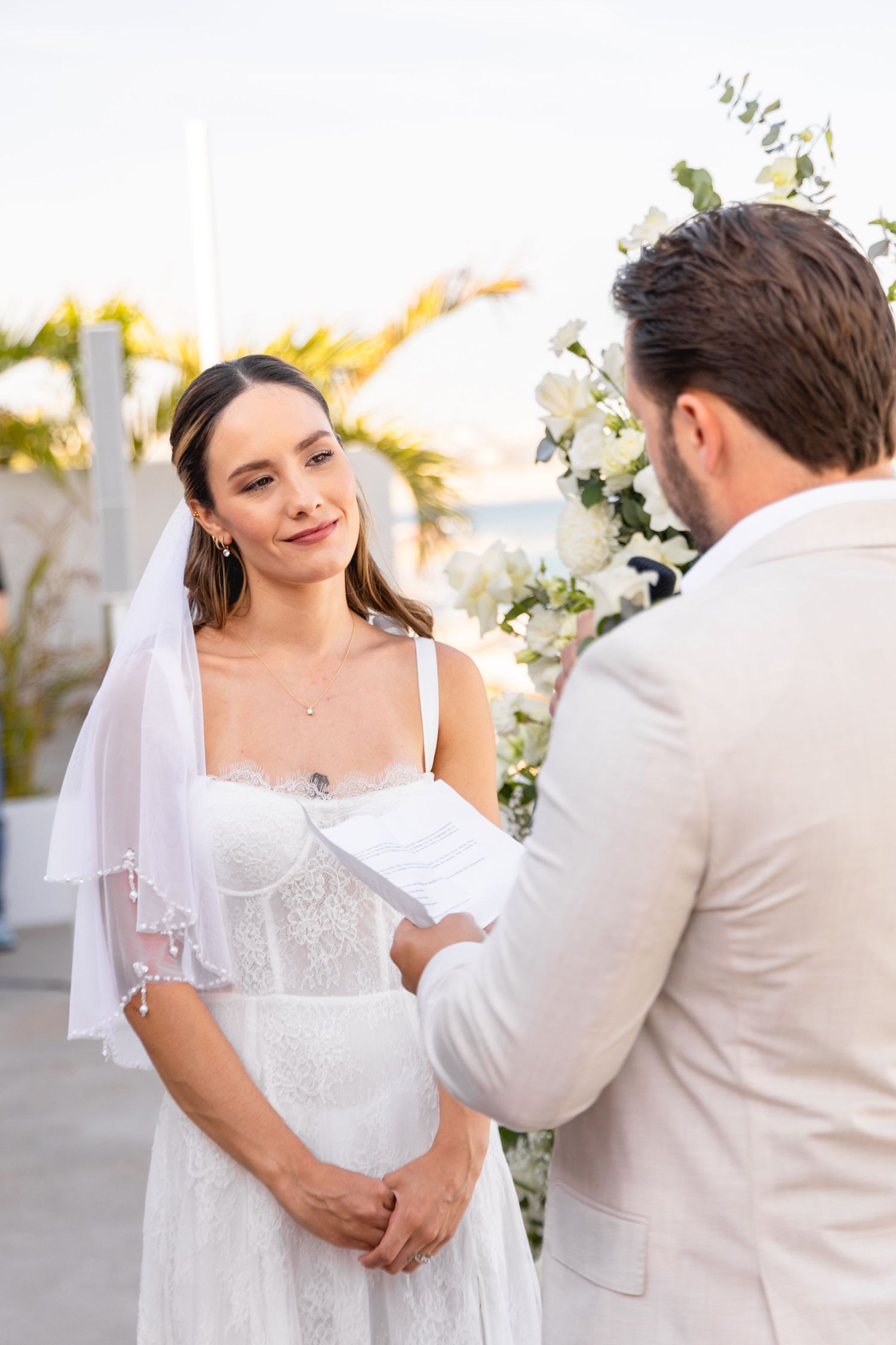 A couple exchanges vows during a wedding ceremony decorated with elegant white floral arrangements.