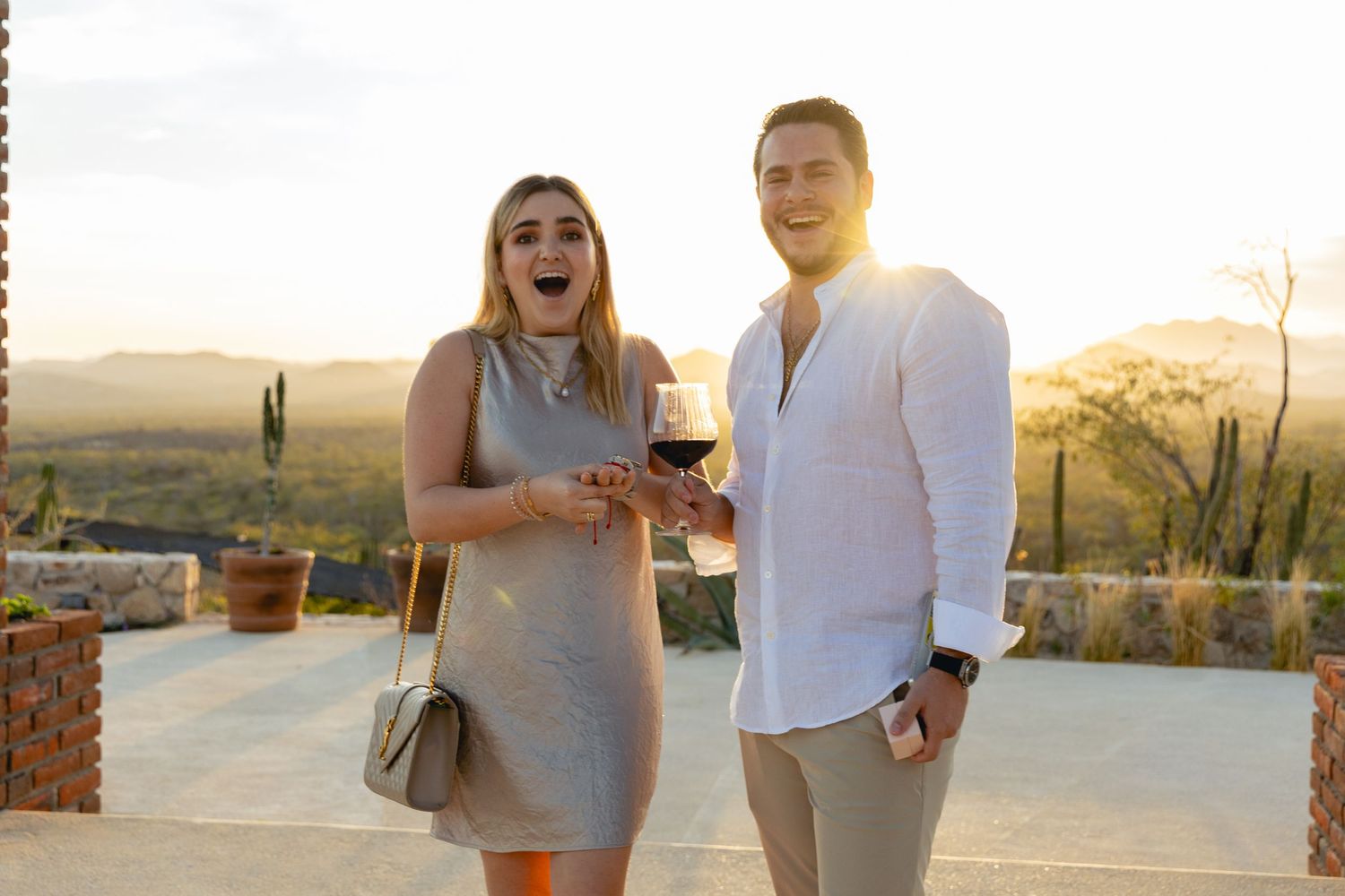 A couple laughs together while walking along a desert path at sunset with saguaro cacti in the background.