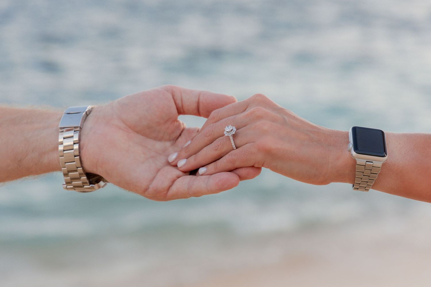 Two hands exchanging a wedding ring against a blurred blue background.