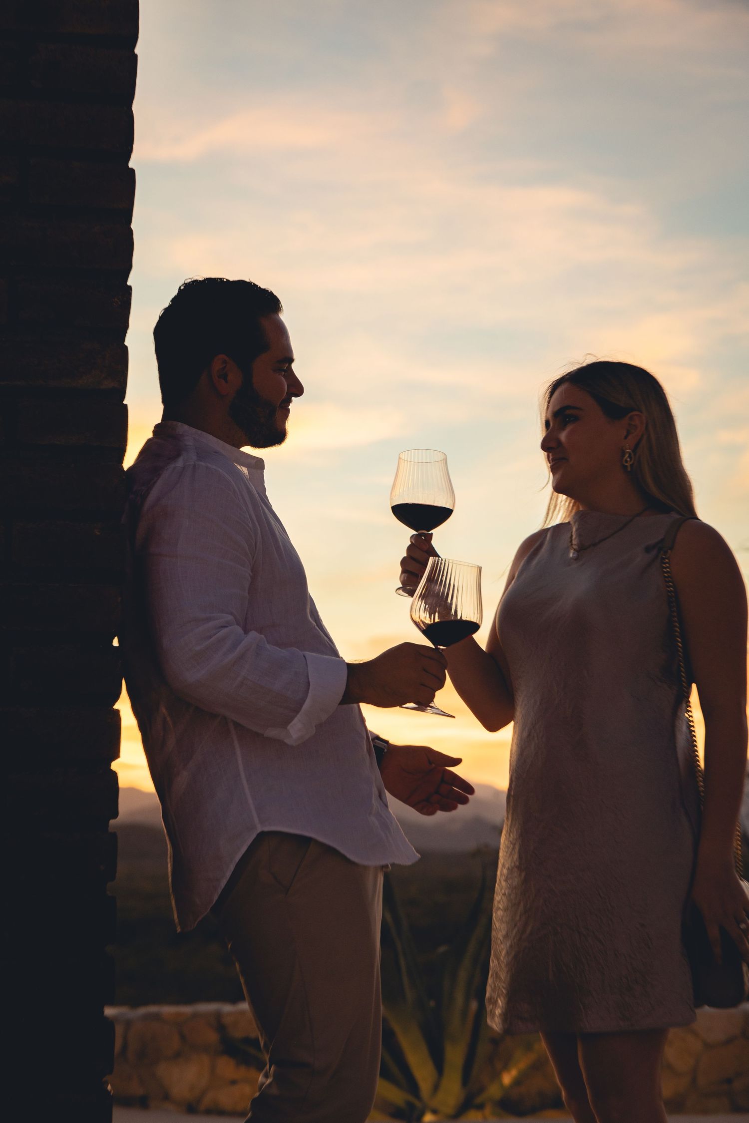 Silhouetted couple sharing wine glasses against a sunset sky during a romantic outdoor moment.
