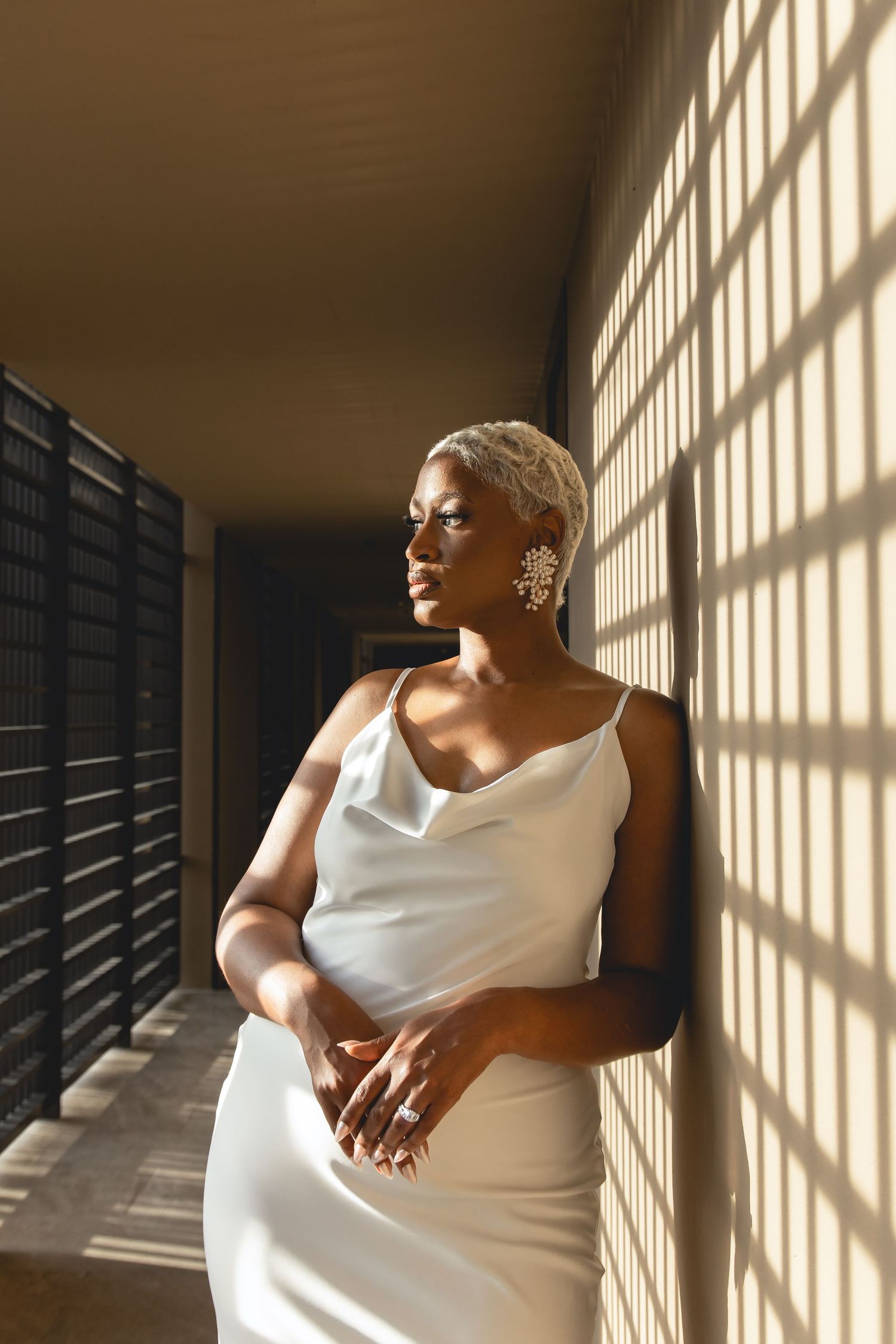 Person in white dress seated by window with dramatic shadow patterns.