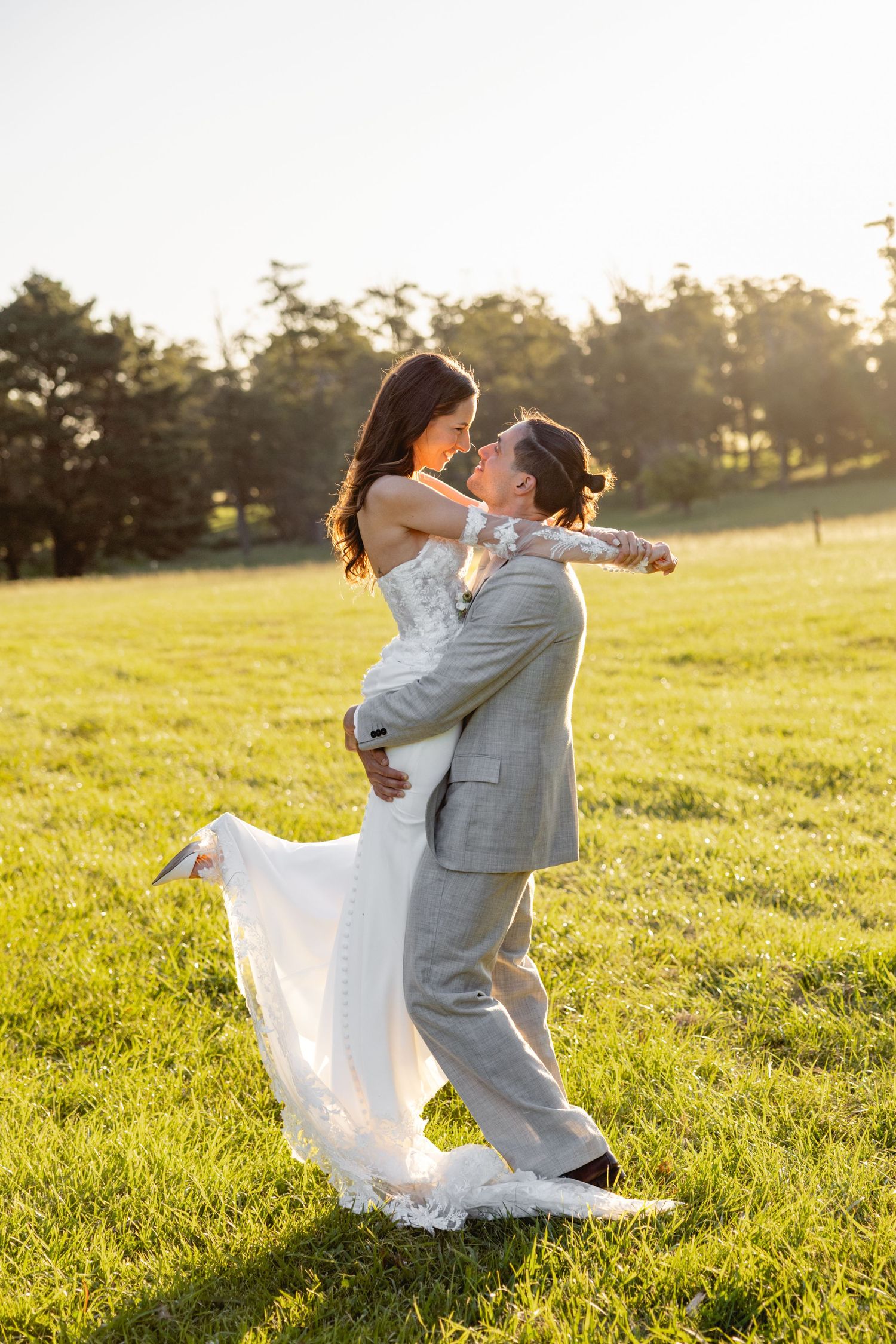 Newlyweds share playful moments in a grassy field bathed in evening sunlight.