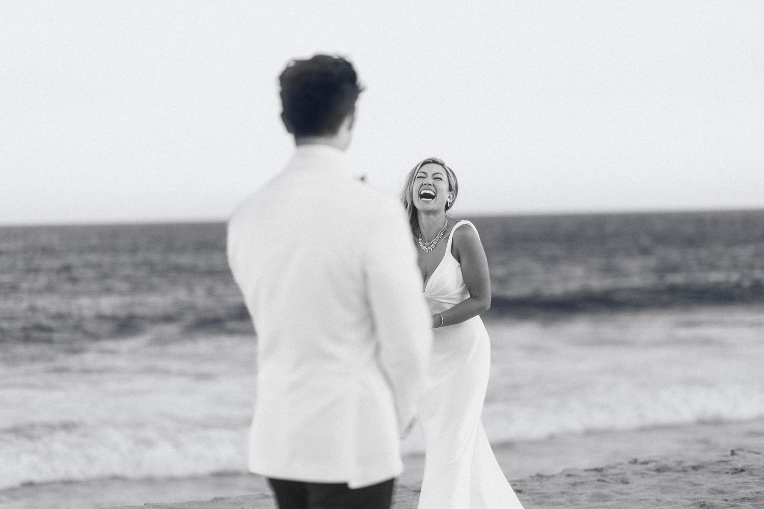 Couple walking hand in hand along beach shoreline in formal wedding attire.