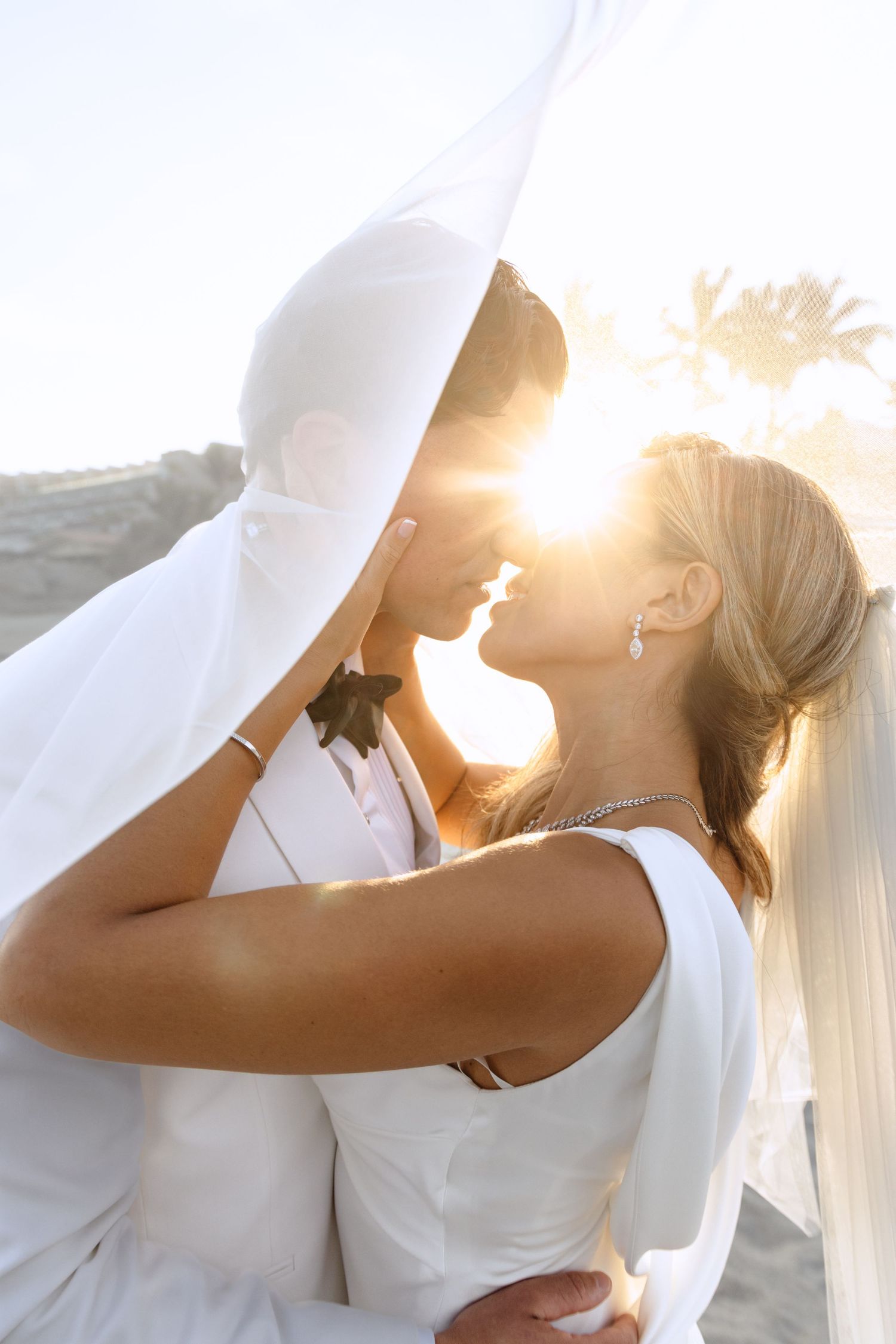 Romantic sunset wedding portrait with couple in white attire and veil.
