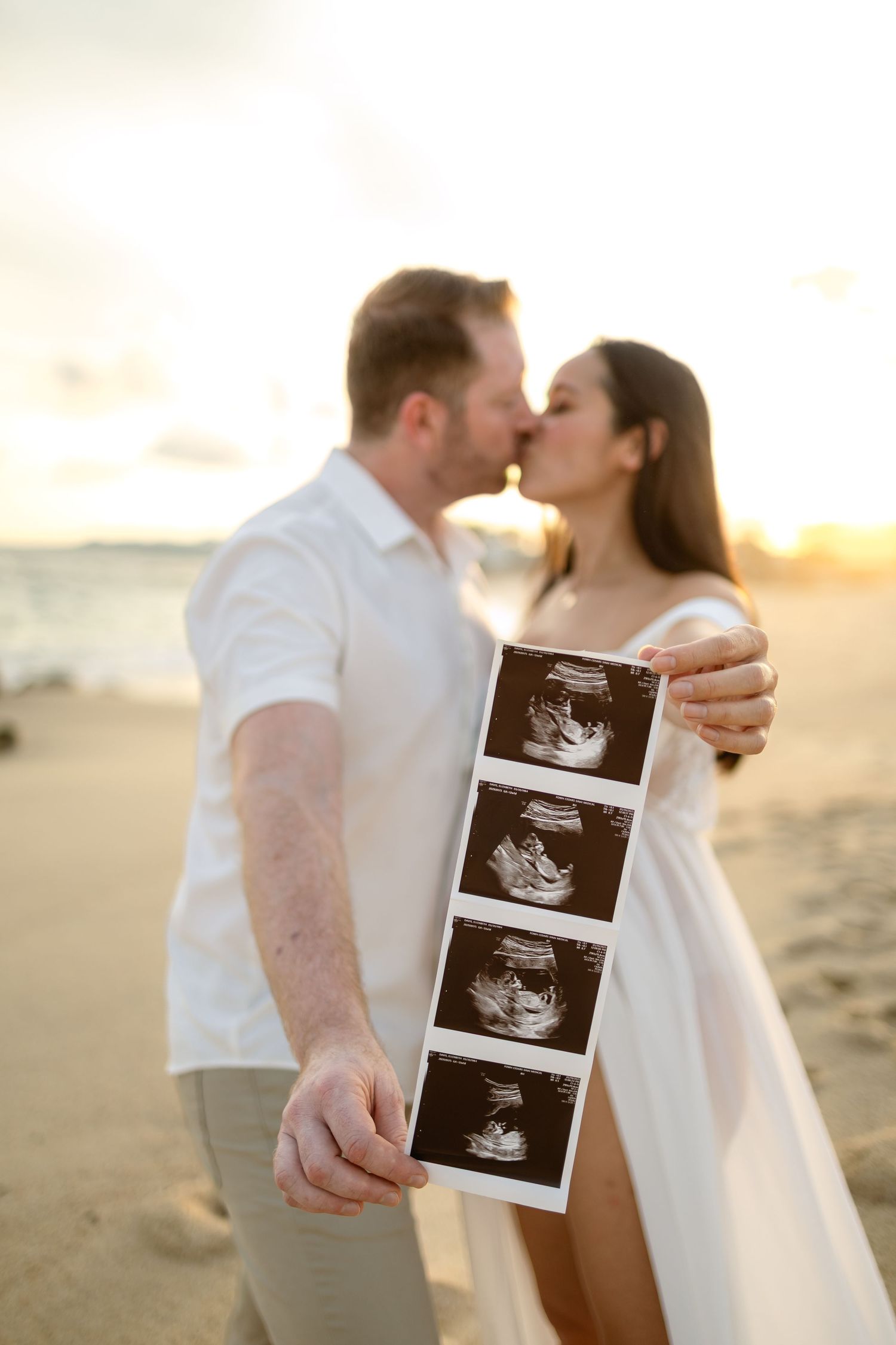 Couple sharing ultrasound photos during sunset beach pregnancy announcement shoot.