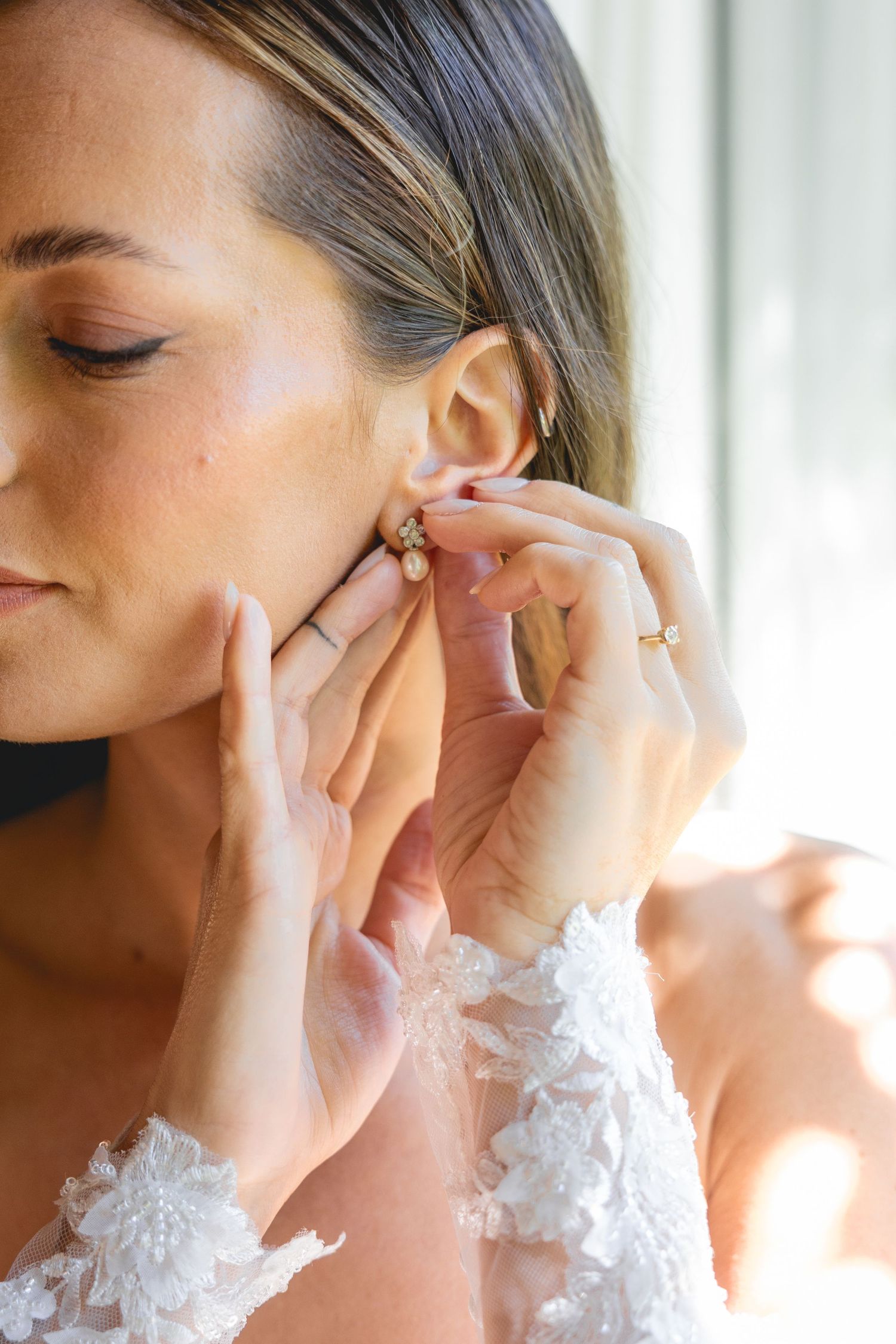 Close-up shot of hands putting on elegant earring with lace detail visible.