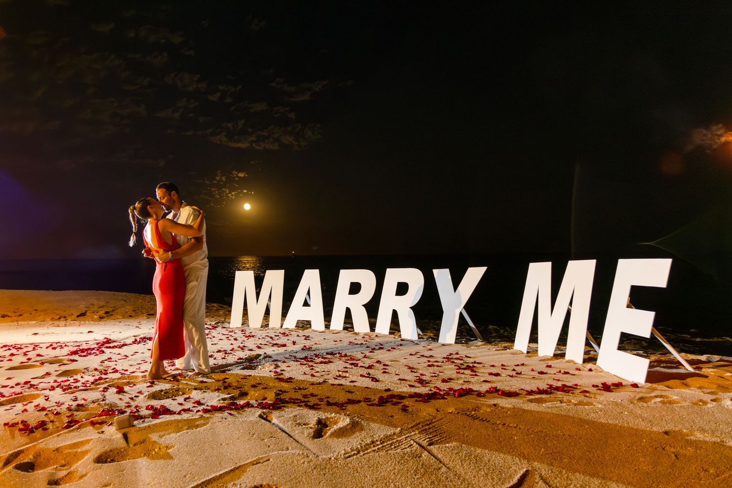 A nighttime marriage proposal scene with illuminated letters spelling 'MARRY ME' against a snowy winter landscape.