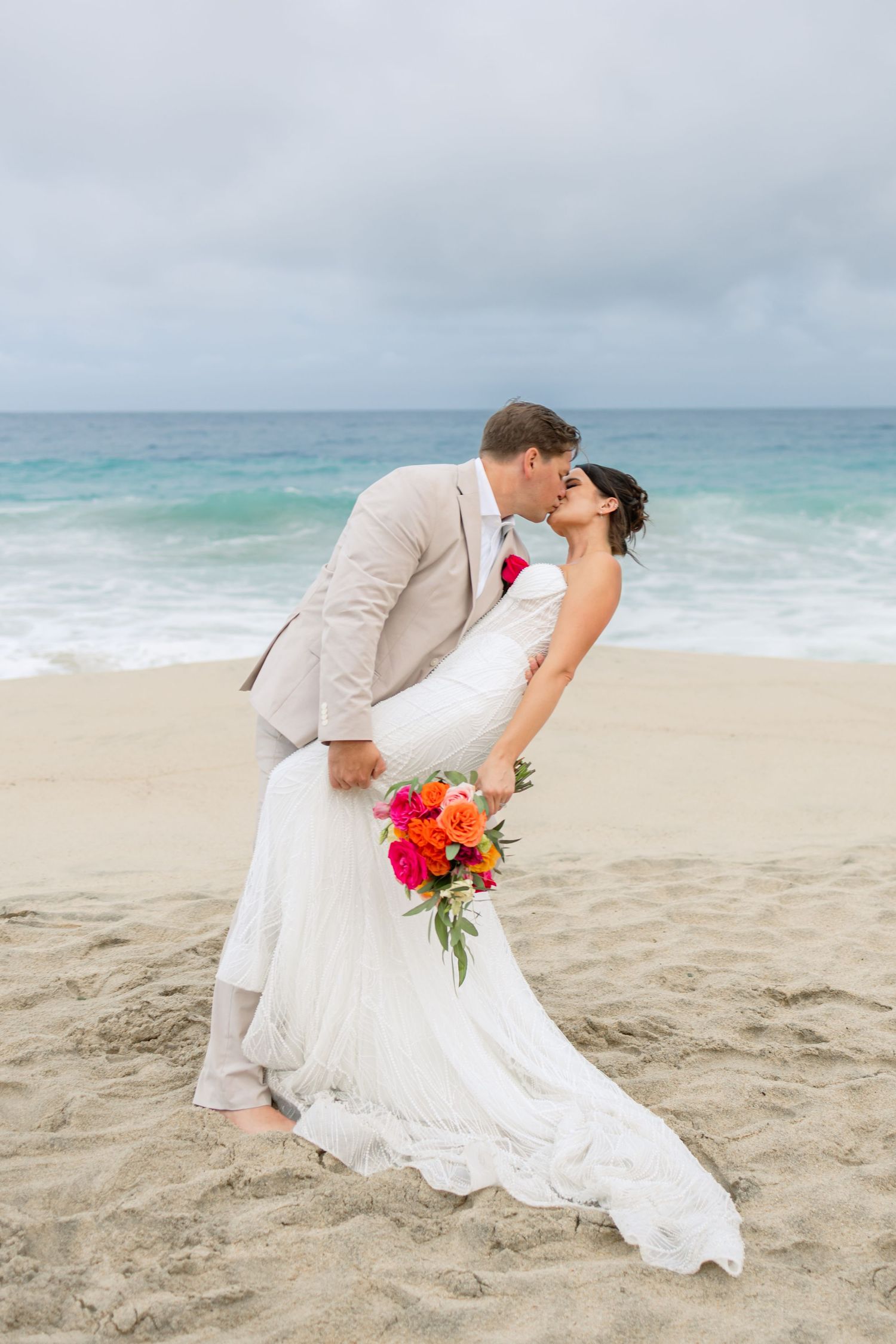 A romantic beach wedding photoshoot with the couple posing in dramatic dips on the sand.