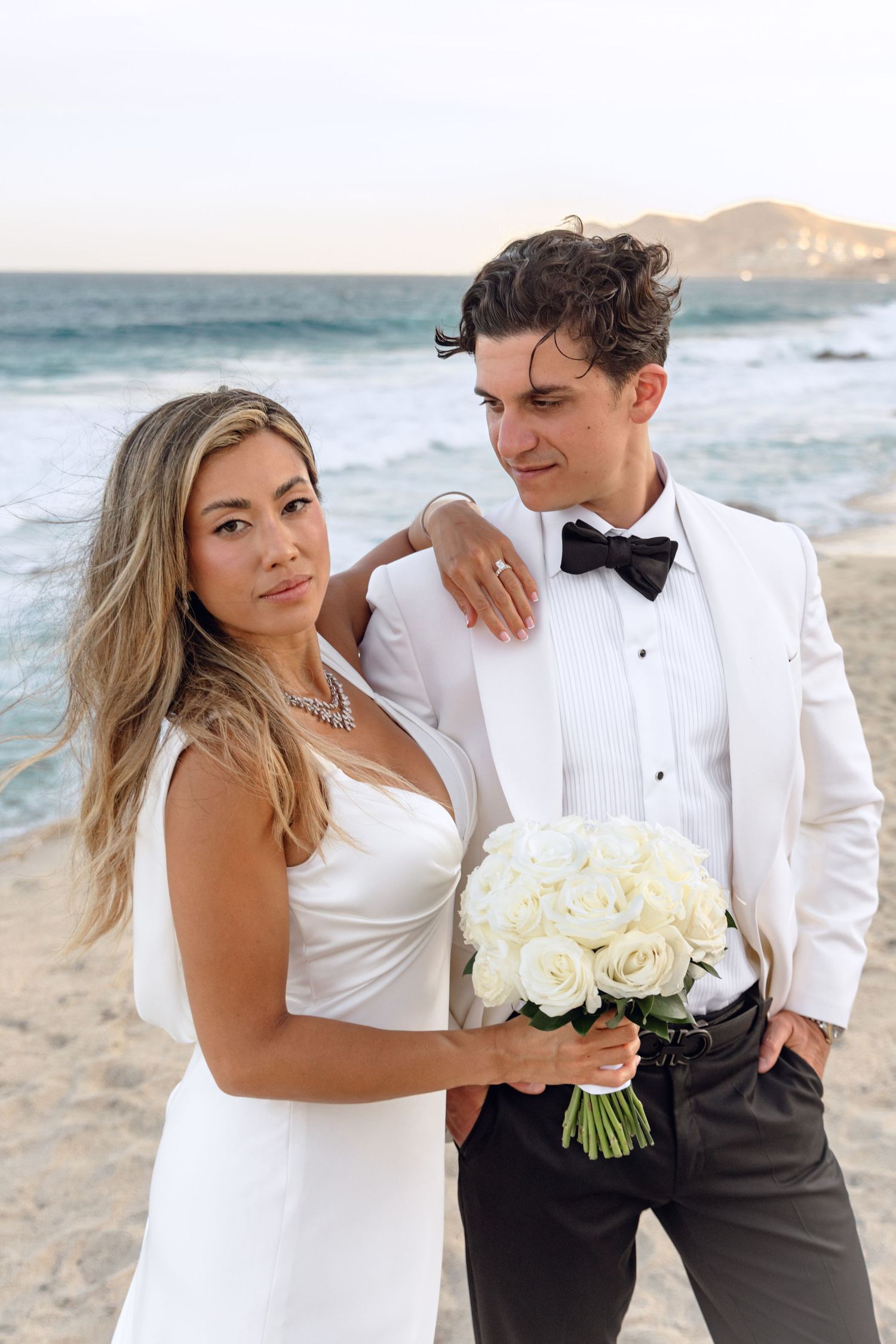 Stylish beach wedding portrait with couple holding white rose bouquet.