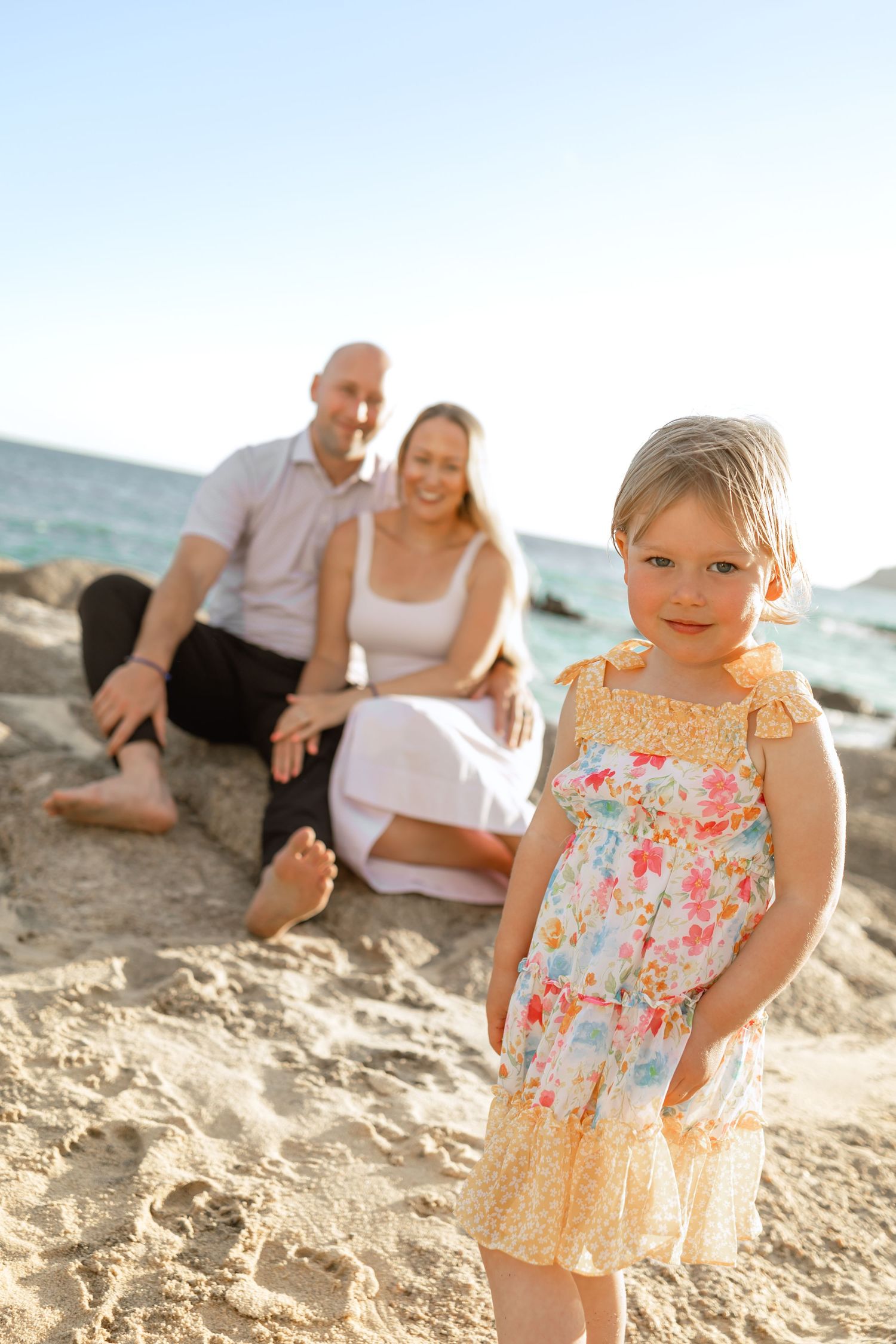 Family enjoying a sunset photoshoot at the beach with young child in floral dress playing in the sand at Garza Blanca, Los Cabos