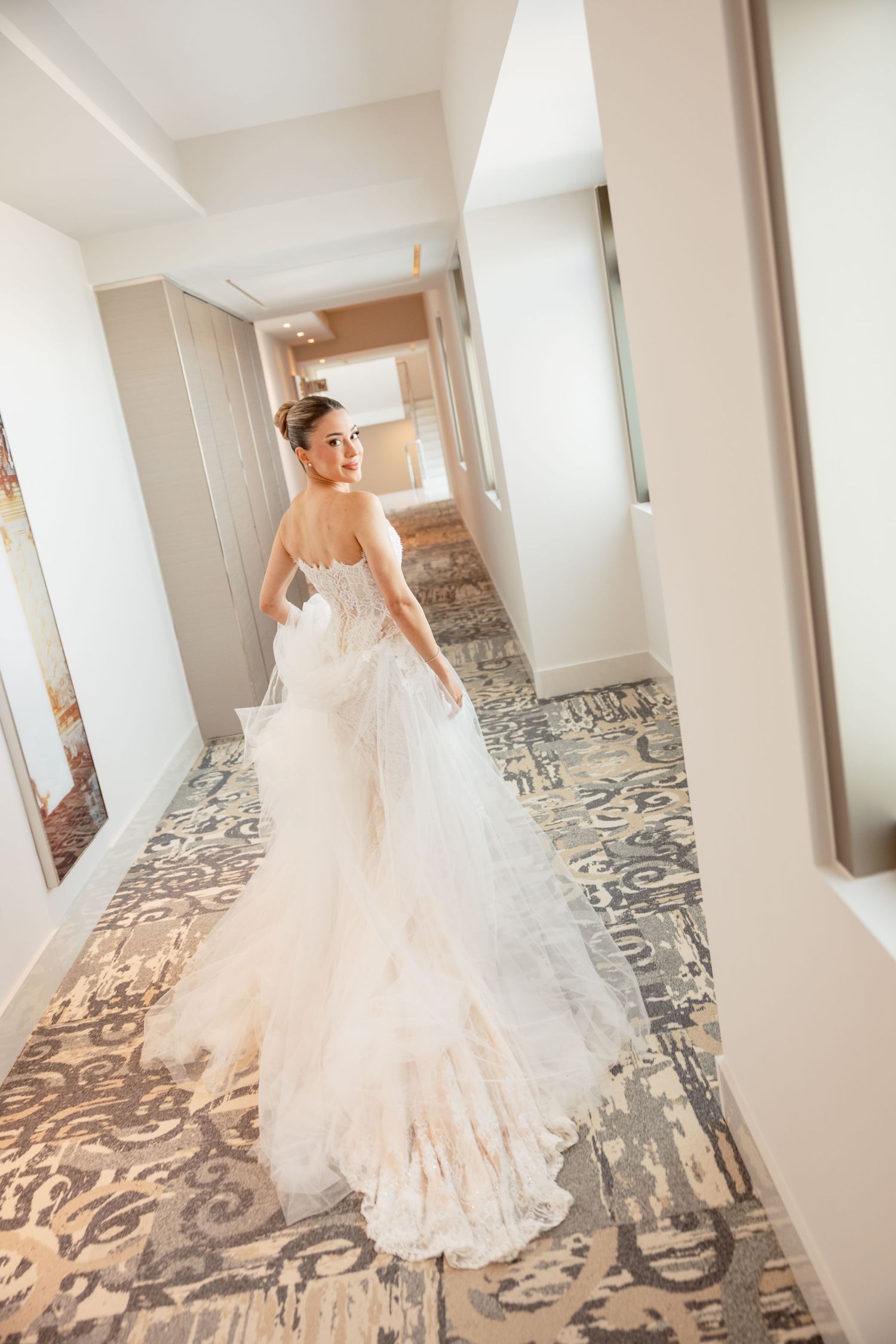 Elegant bridal portraits showcasing the flowing train of a lace wedding gown in a hotel hallway.