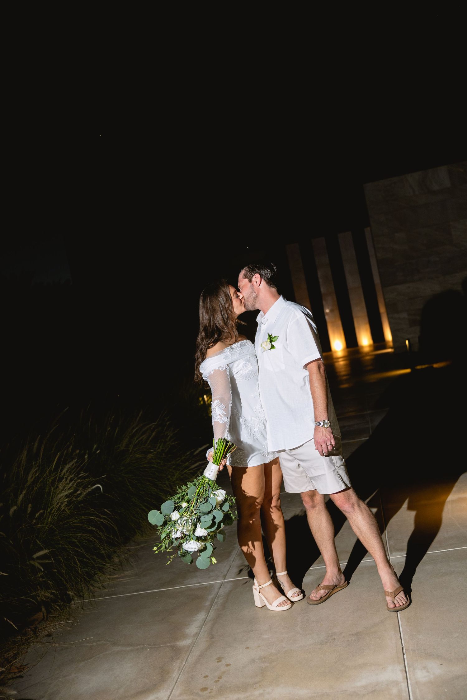 Couple in matching white outfits walking together at night with decorative lighting.
