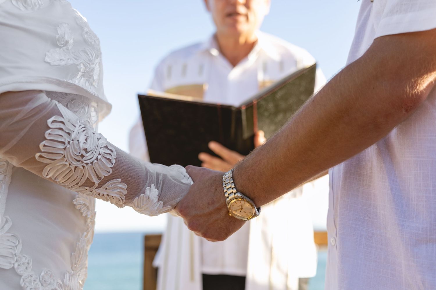 Close-up of hands during a wedding ceremony on an oceanfront deck.