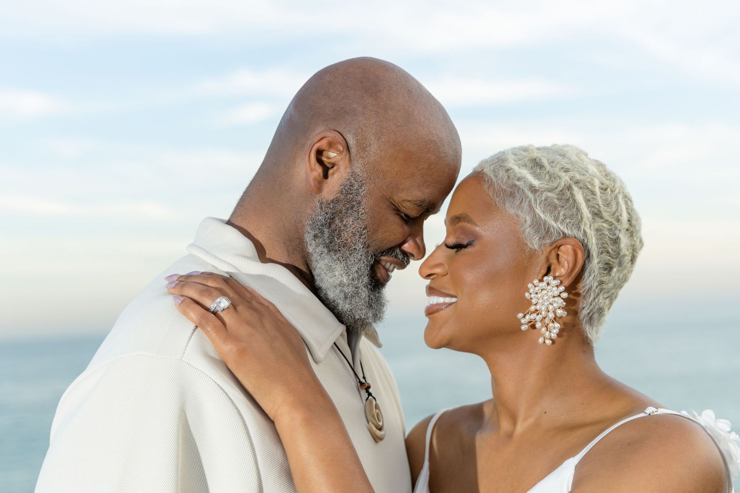 A romantic beach wedding photoshoot with a couple in white attire embracing against an ocean backdrop.