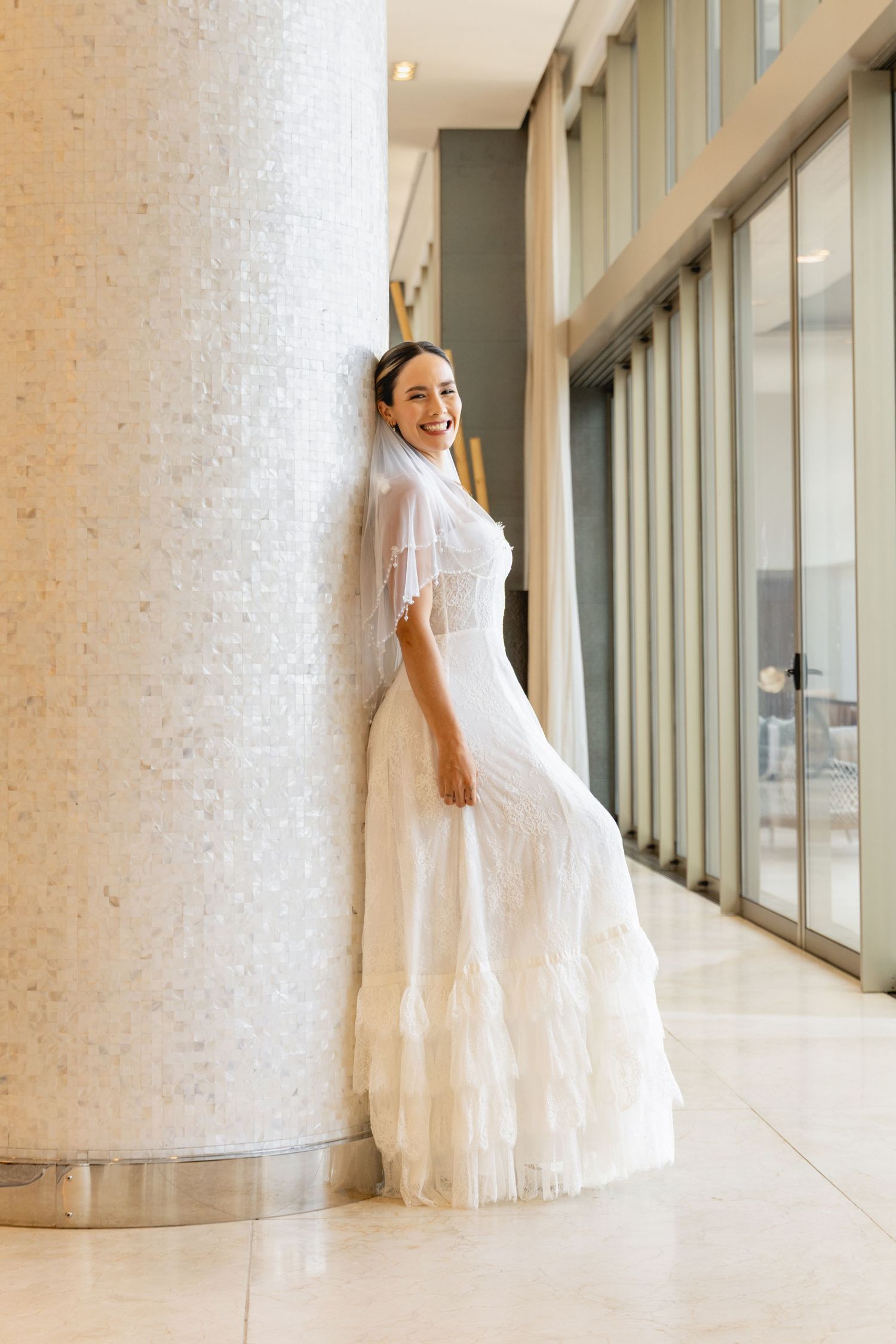 Elegant white wedding dress flowing against modern architectural columns and glass windows.