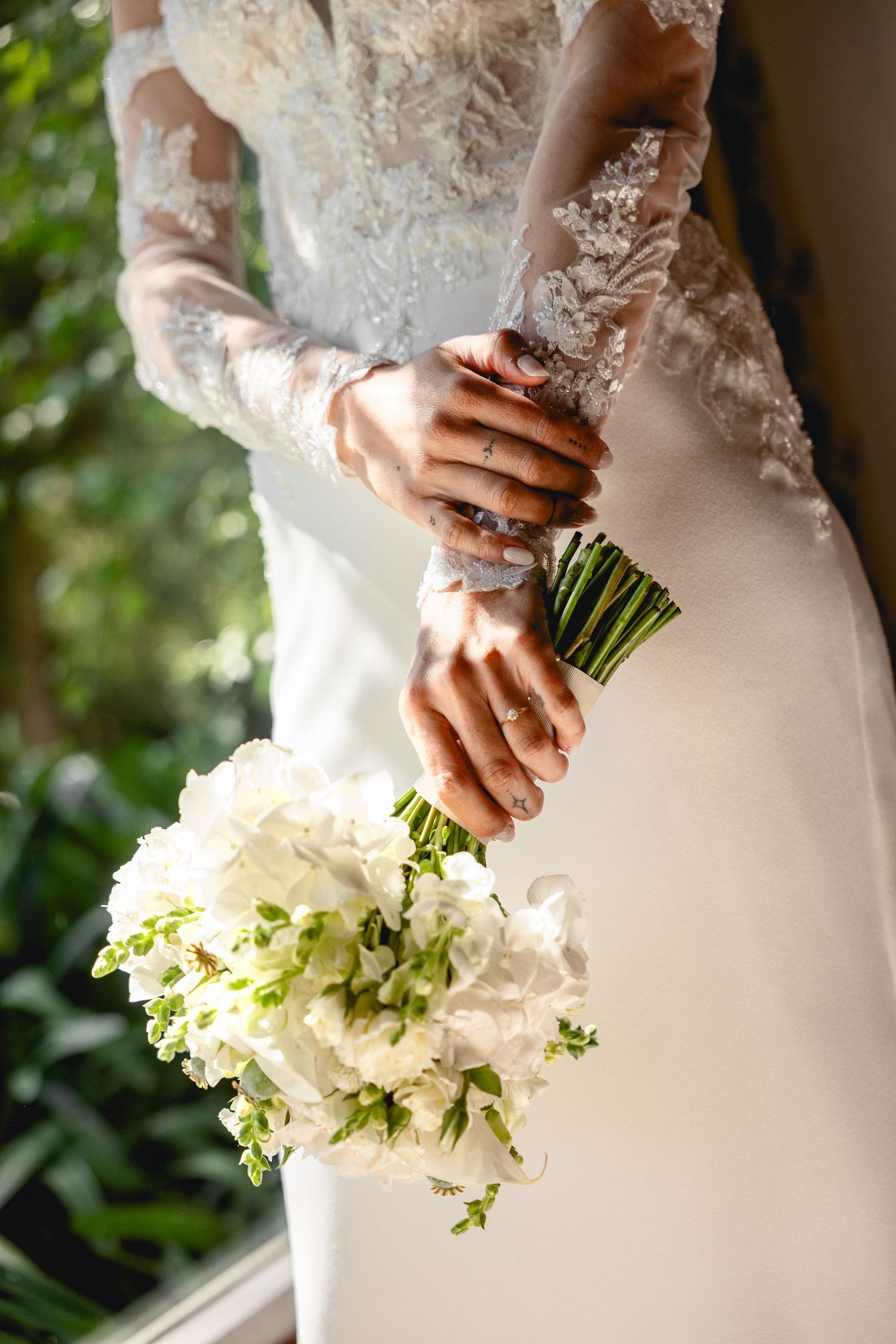 Close-up of delicate lace sleeves and white floral bouquet against wedding dress.