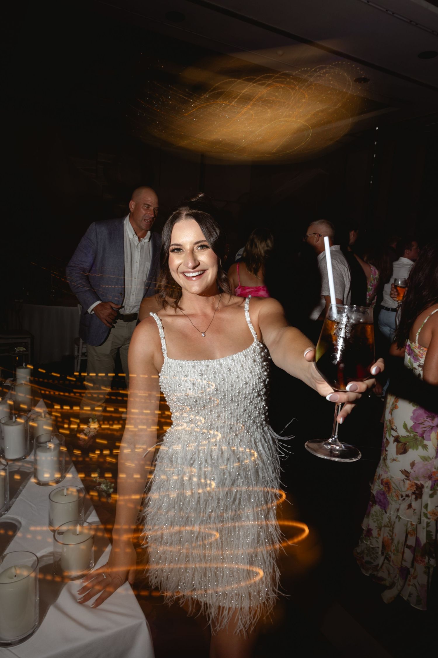 Bride in a sparkly white dress dances joyfully at a wedding reception with twinkling lights in the background.