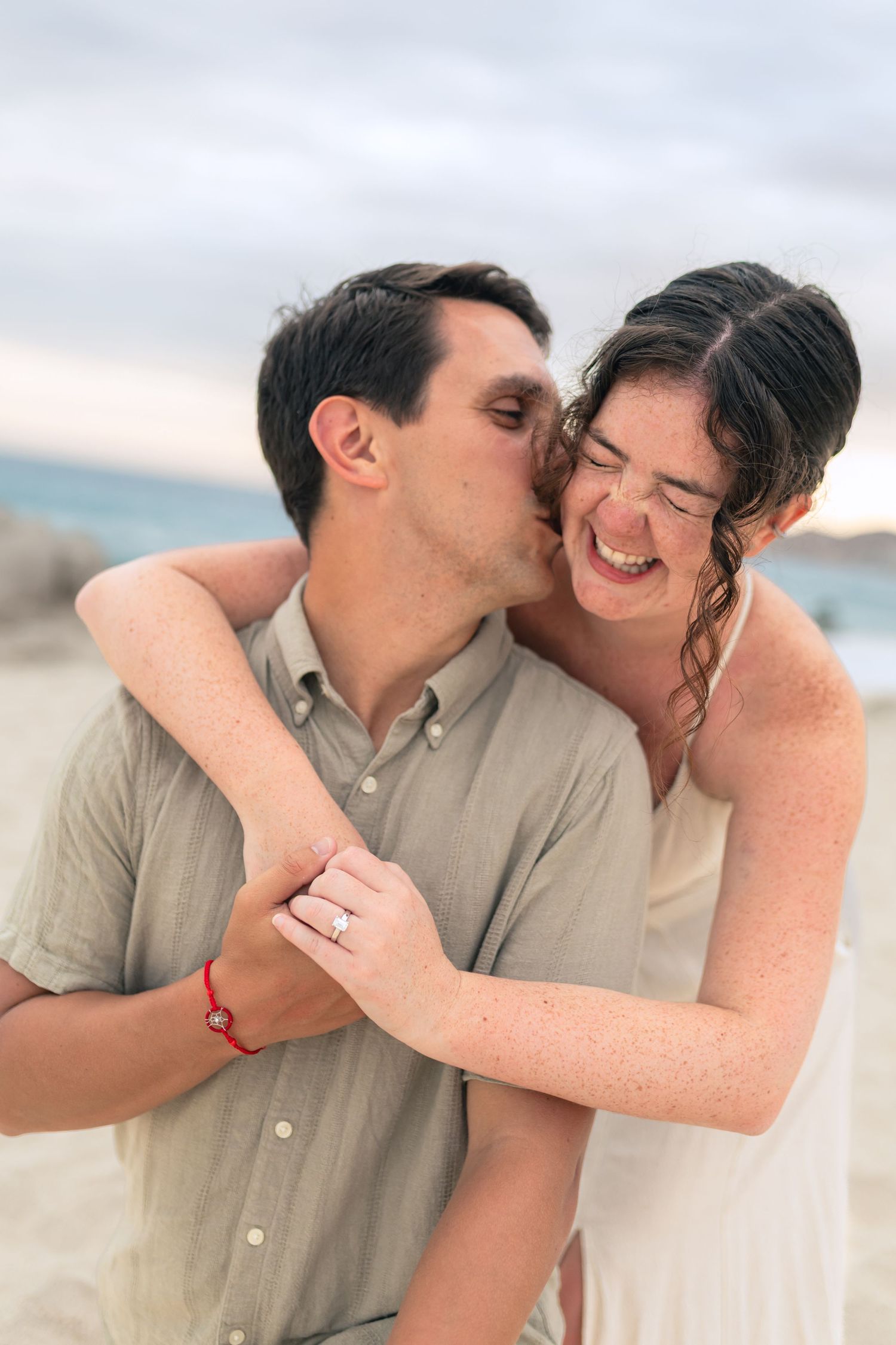 A romantic couple shares a tender moment and laugh together on a beach at sunset.