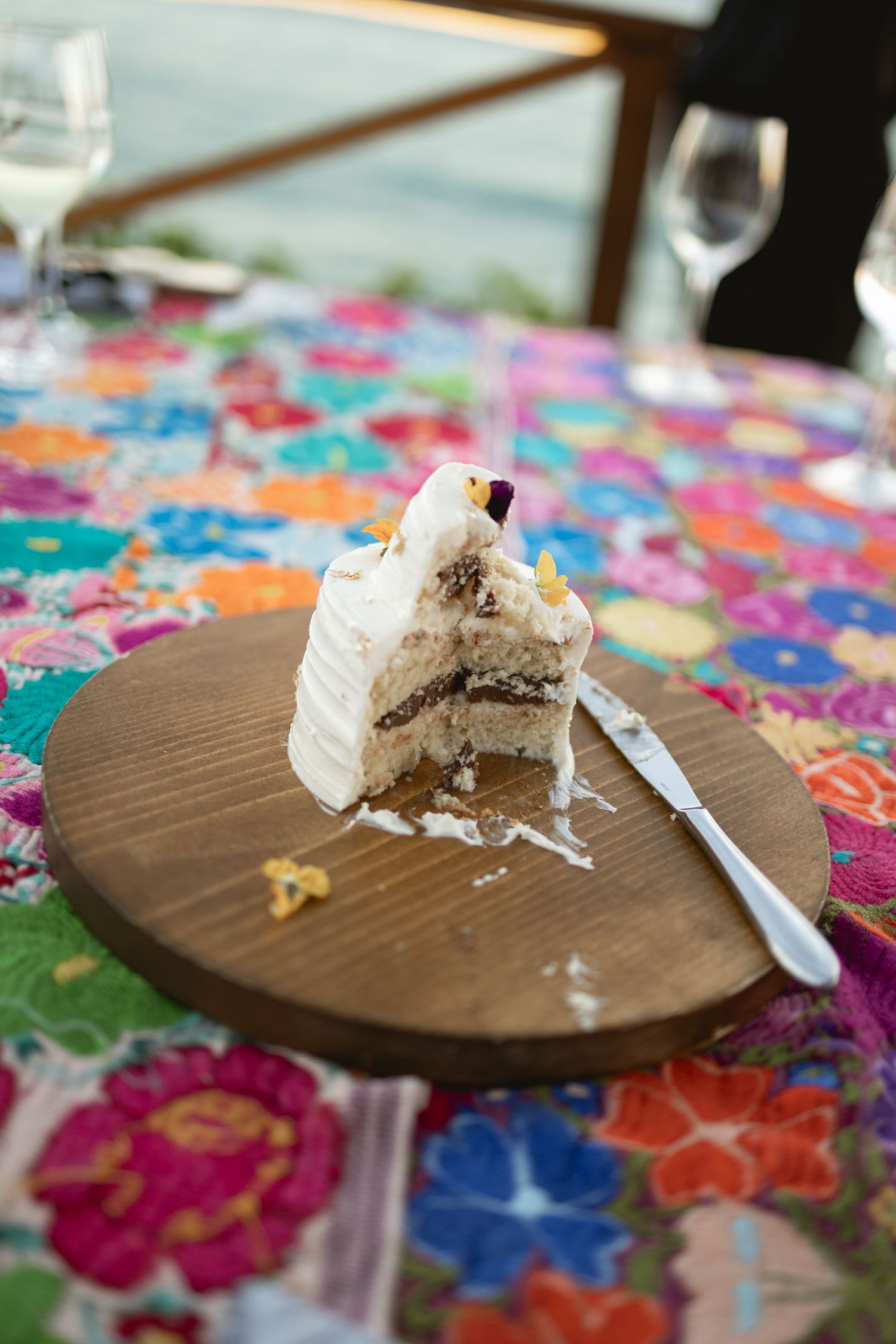 A slice of white wedding cake with layers on a colorful floral tablecloth.